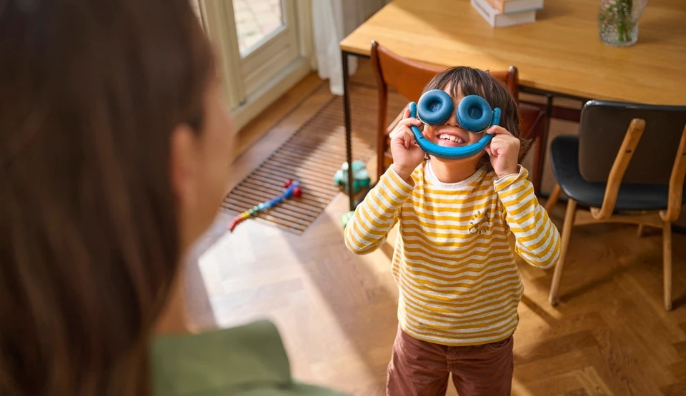 Chłopiec zakłada słuchawki na oczy, uśmiechając się.