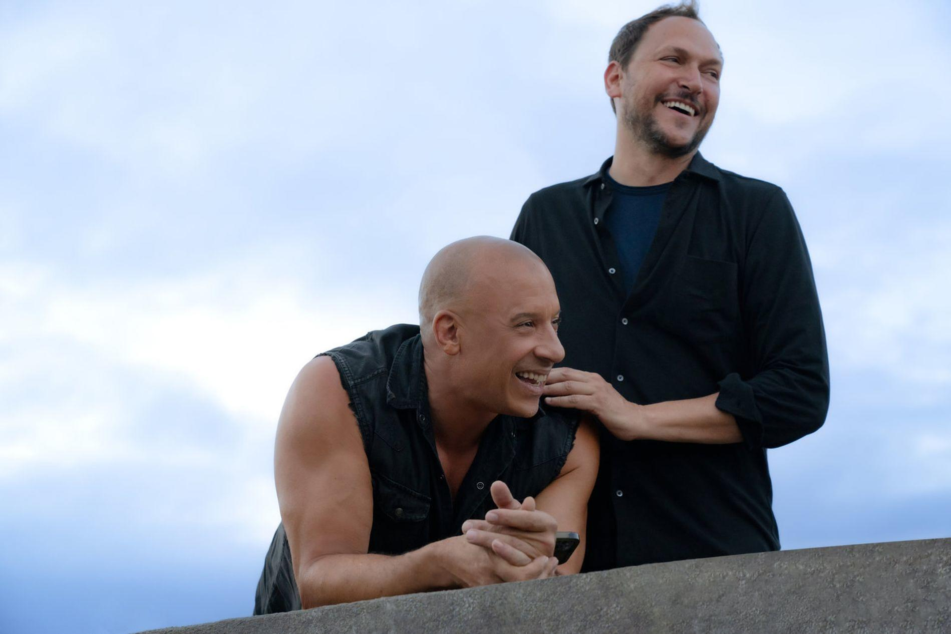 Zwei Männer lachen, einer mit Glatze, der andere mit Bart. Blauer Himmel im Hintergrund.
