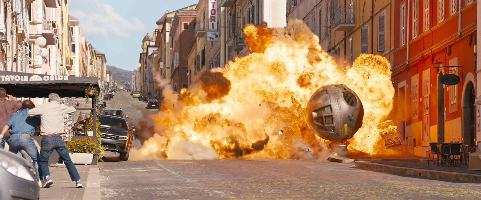 Eine riesige Explosion auf einer Straße mit Gebäuden und Menschen, die sich ducken.