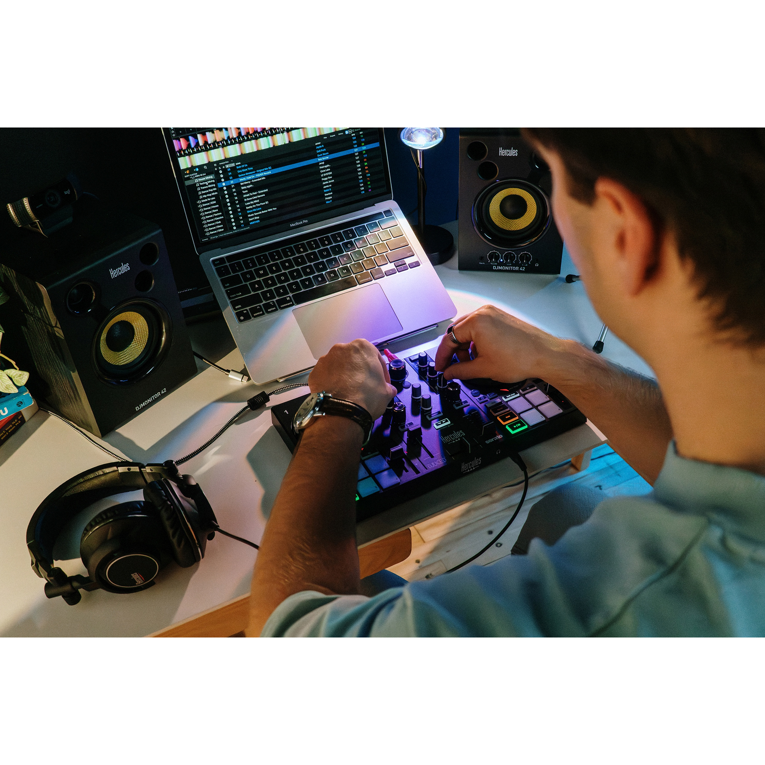 Een man bedient een DJ-controller voor een laptop, met luidsprekers en koptelefoon in de buurt.