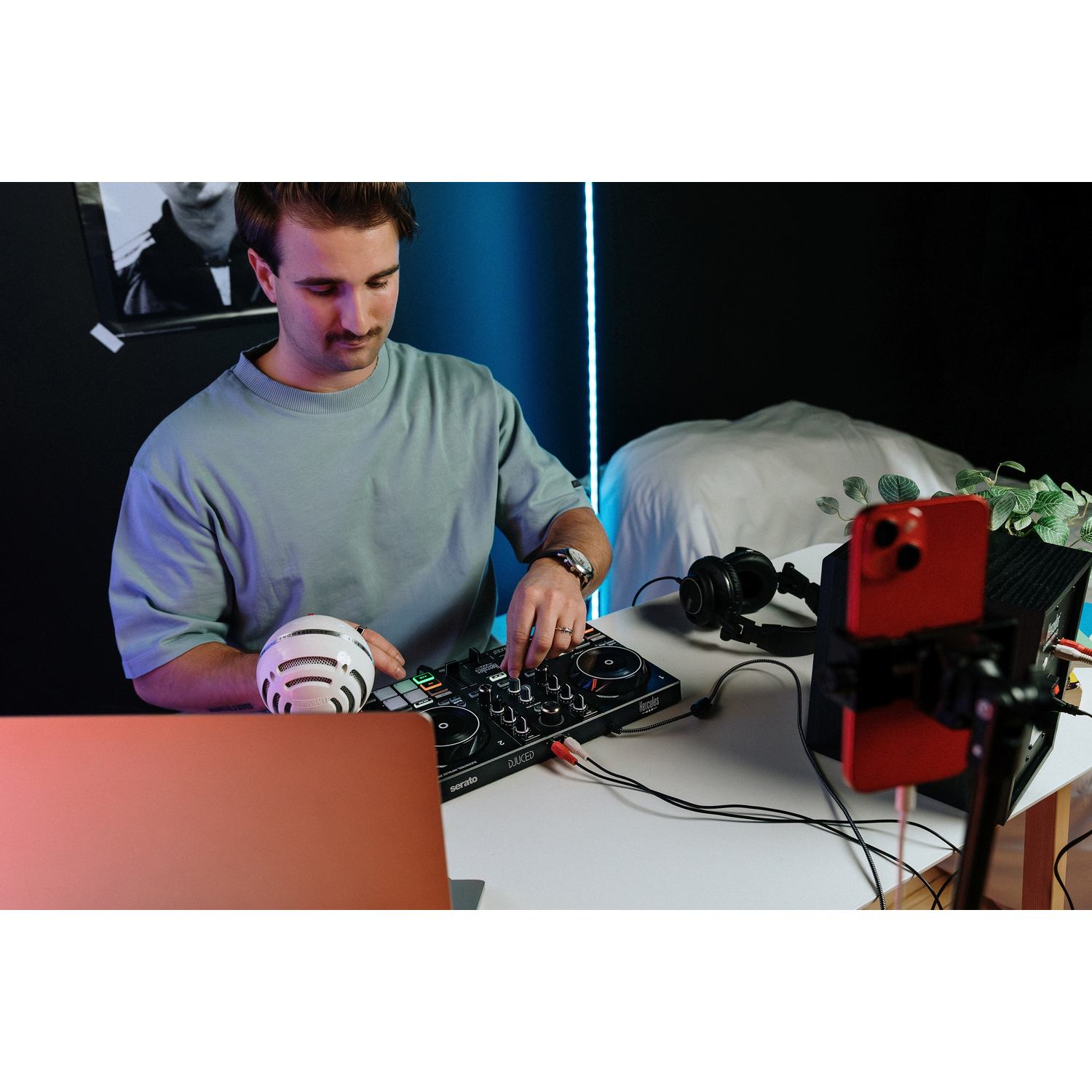 Een man zit aan een DJ-console met laptop, microfoon, koptelefoon en smartphone.