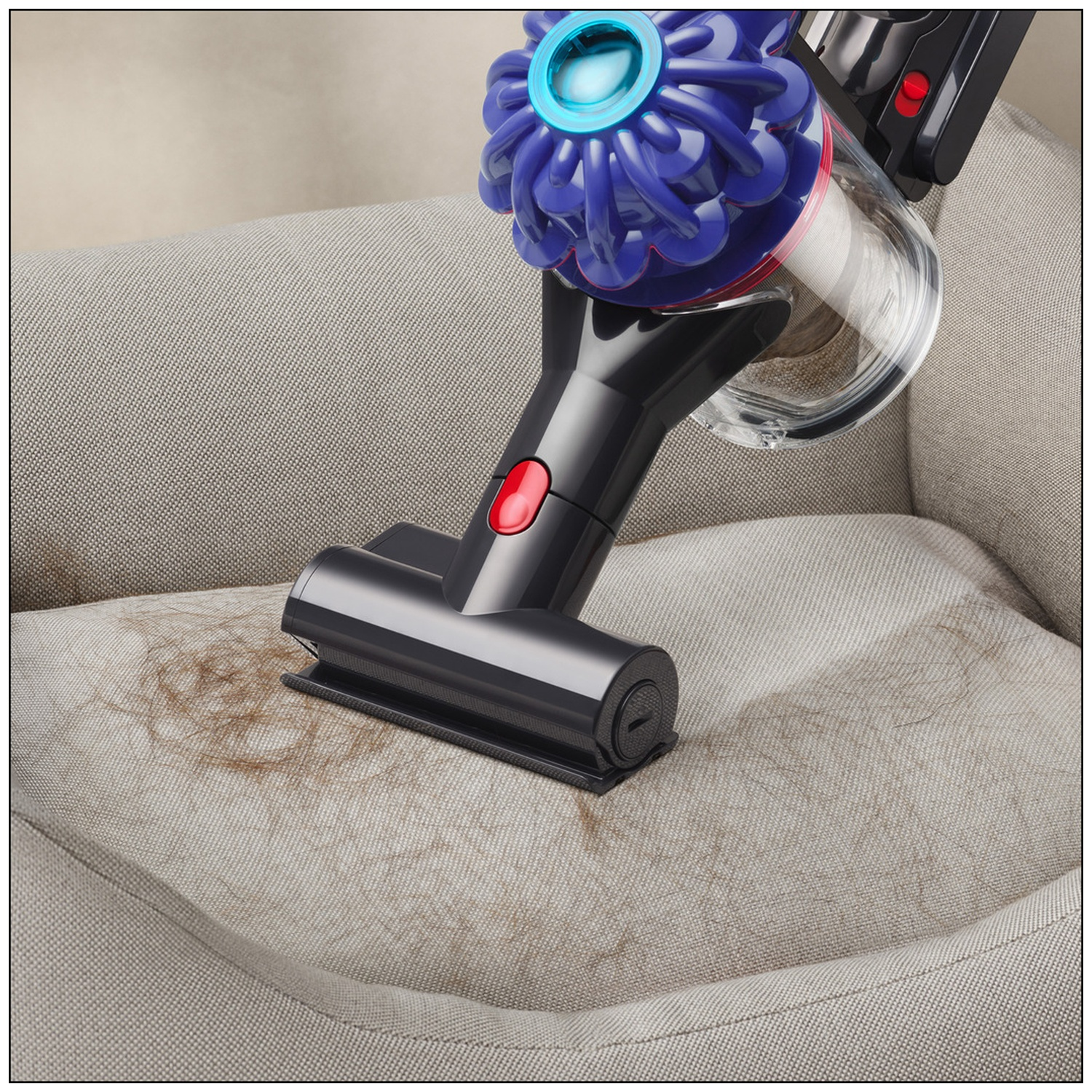 Un aspirateur nettoie des poils bruns d'un fauteuil en tissu gris clair.