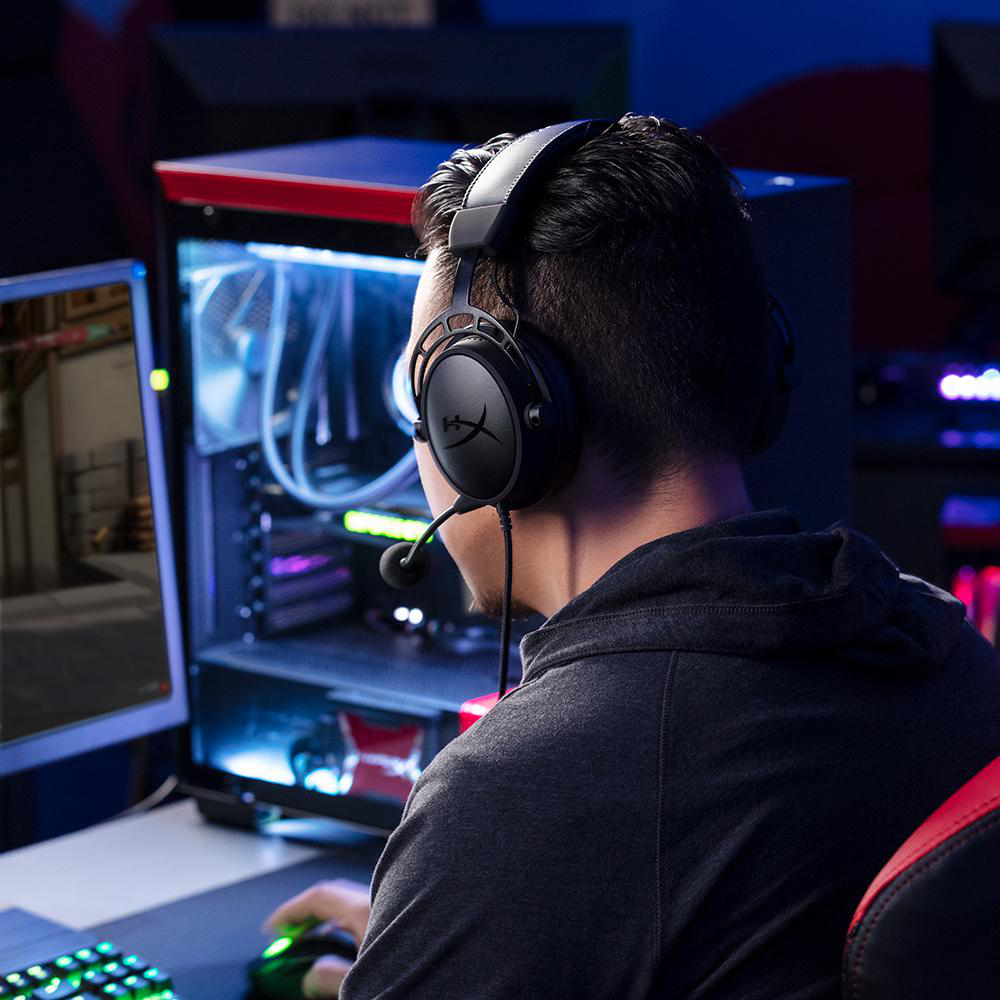 Mann mit Kopfhörern spielt am PC, beleuchtet von blauem und rotem Licht.