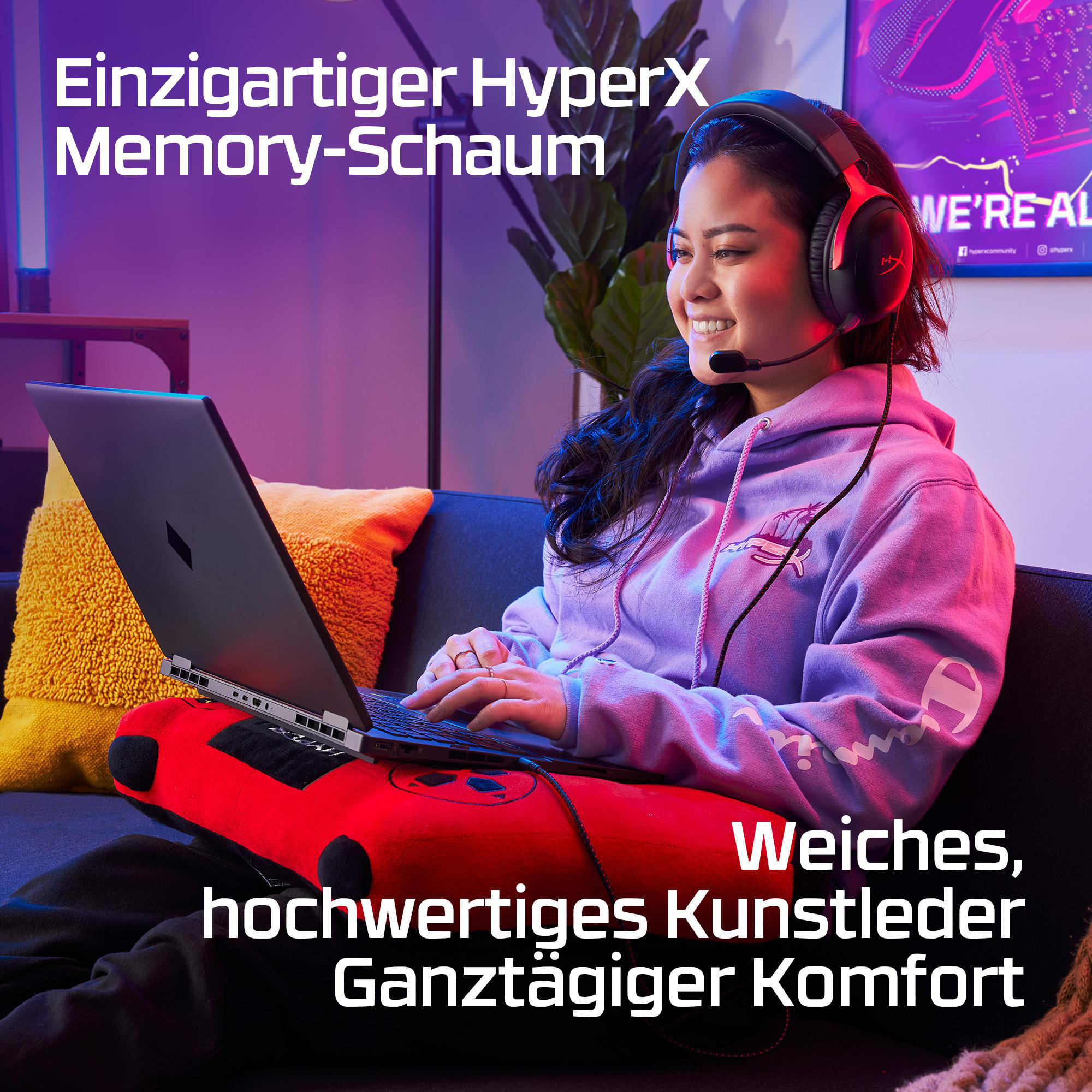 Frau mit Kopfhörern tippt auf Laptop, sitzt auf Sofa mit rotem Kissen.