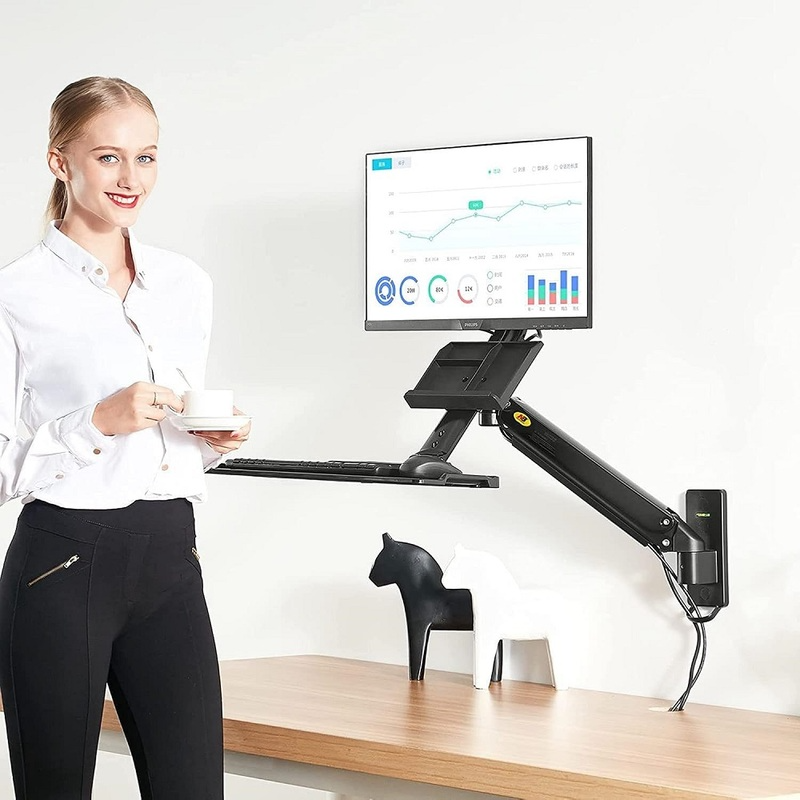Fehér blúzban lévő nő kávésbögrét tart az asztalnál, monitor tartókarral és billentyűzettel.