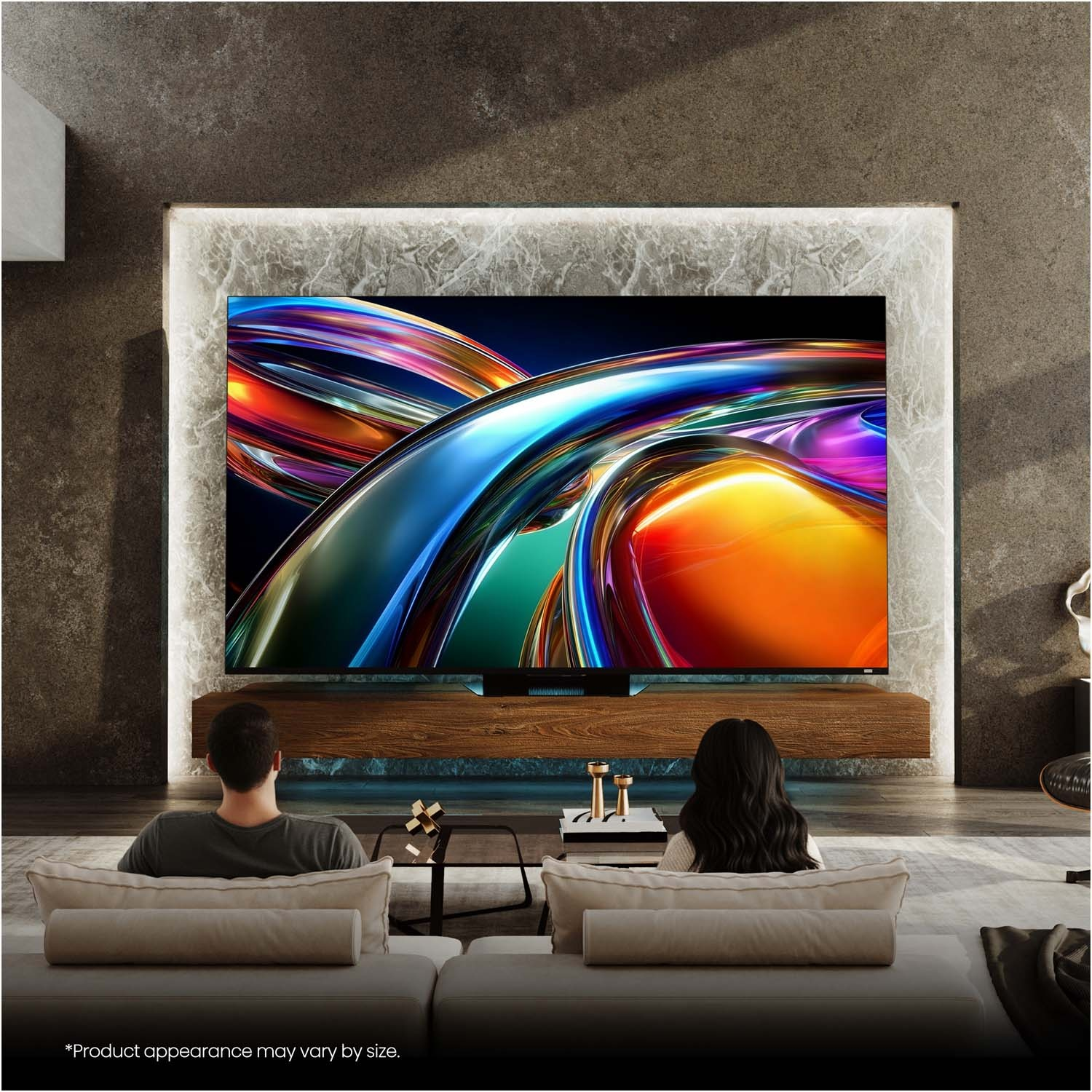 Una coppia seduta sui divani guarda un grande televisore con un'immagine astratta colorata.