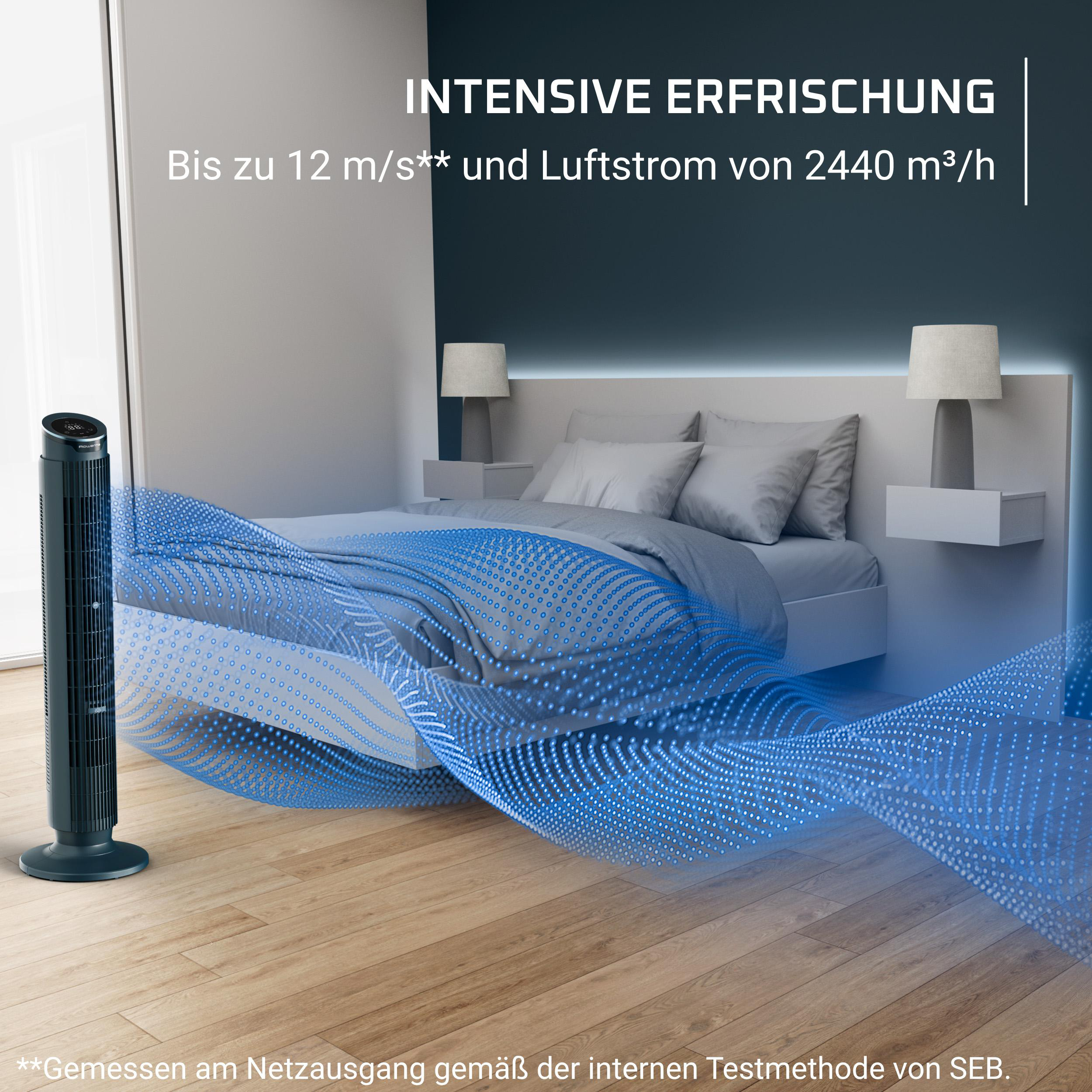 Ein schwarzer Turmventilator steht auf einem Holzboden neben einem Bett.