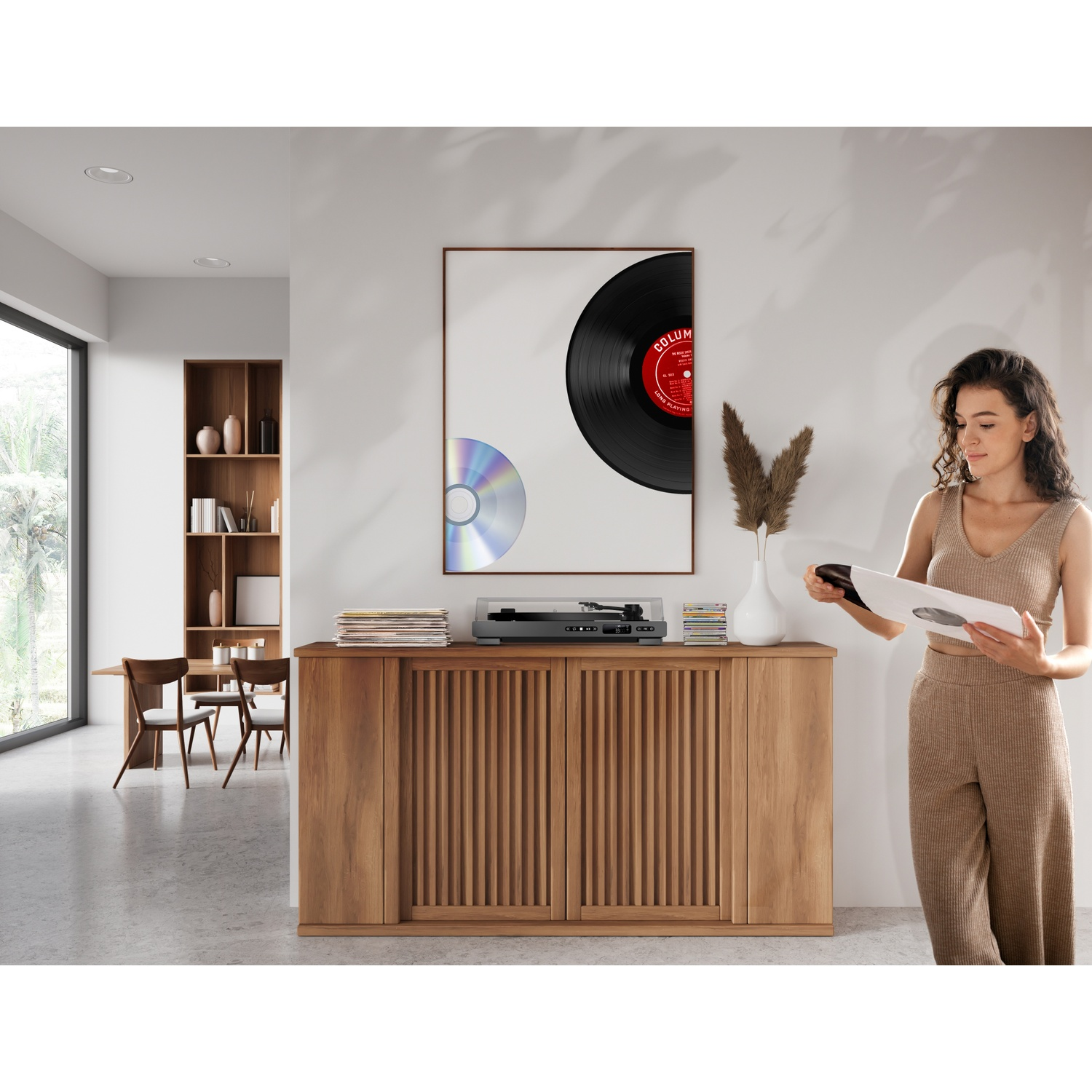 Femme tenant un disque vinyle; tourne-disque et CD sur meuble en bois; salle à manger fond.