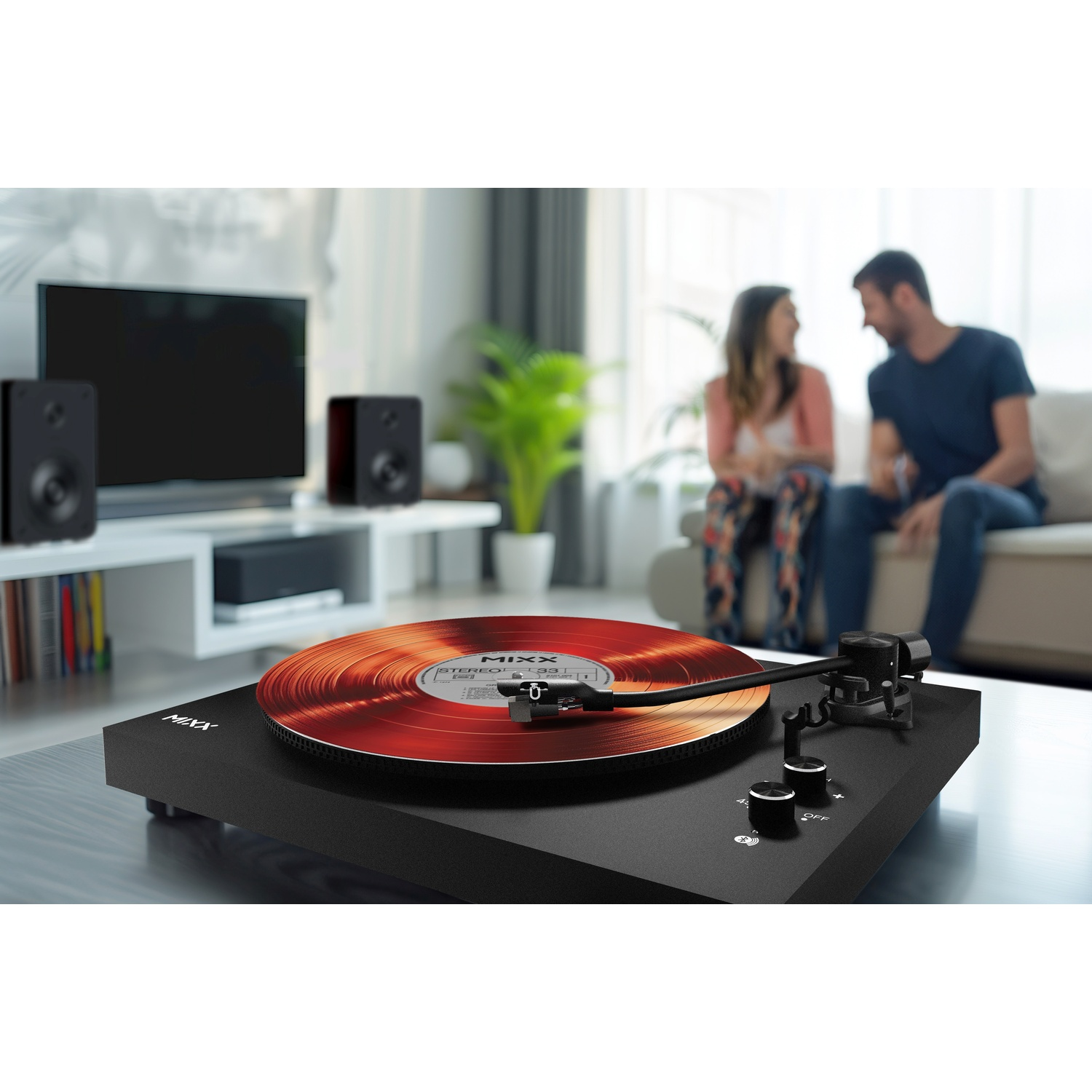 Een zwarte platenspeler met rode vinylplaat speelt in een woonkamer. Paar zit op bank.