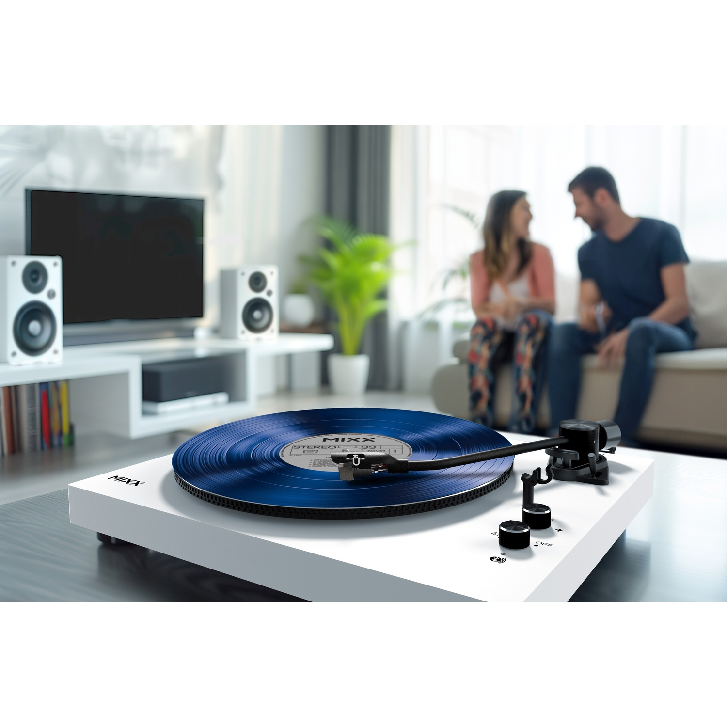 Een witte platenspeler met blauwe plaat speelt muziek, een stel zit op de achtergrond.