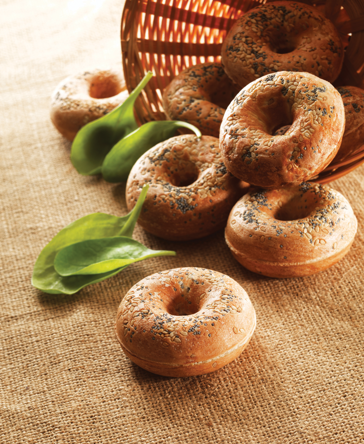 Több magvas bagel, mellette spenót egy kosárban, juton.