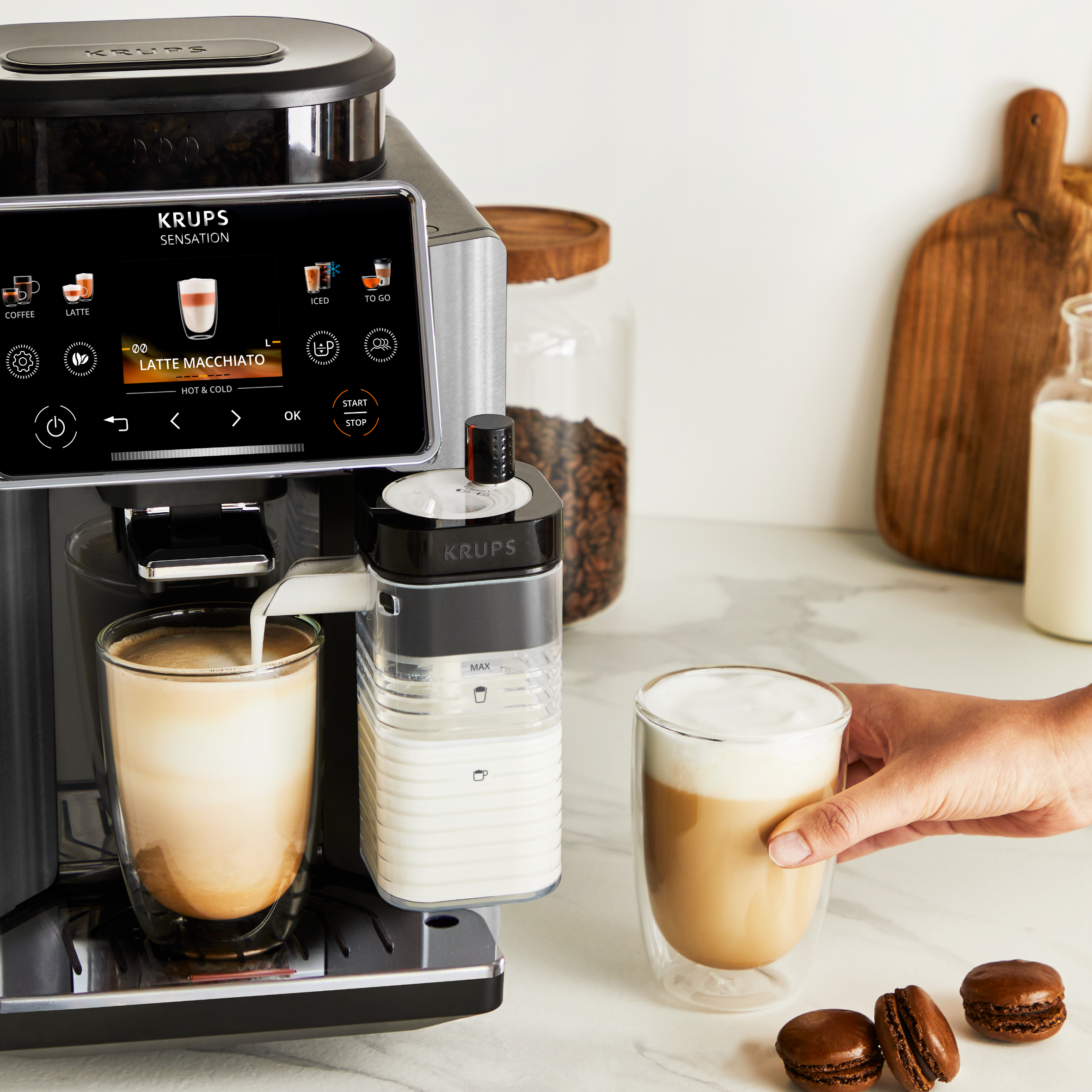 Egy kávéfőző latte macchiato-t készít egy pohárba. Mellette tejtartó.