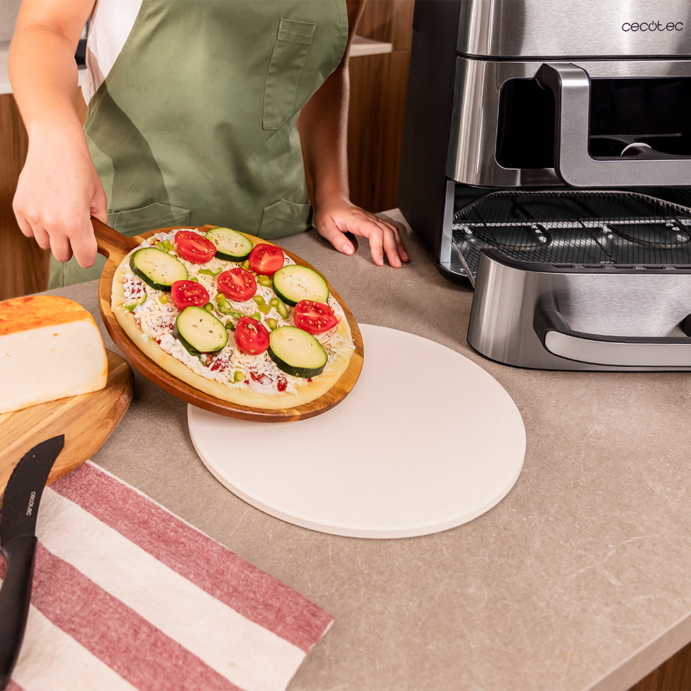 Una pizza sin terminar con tomates y calabacín en una pala de madera.