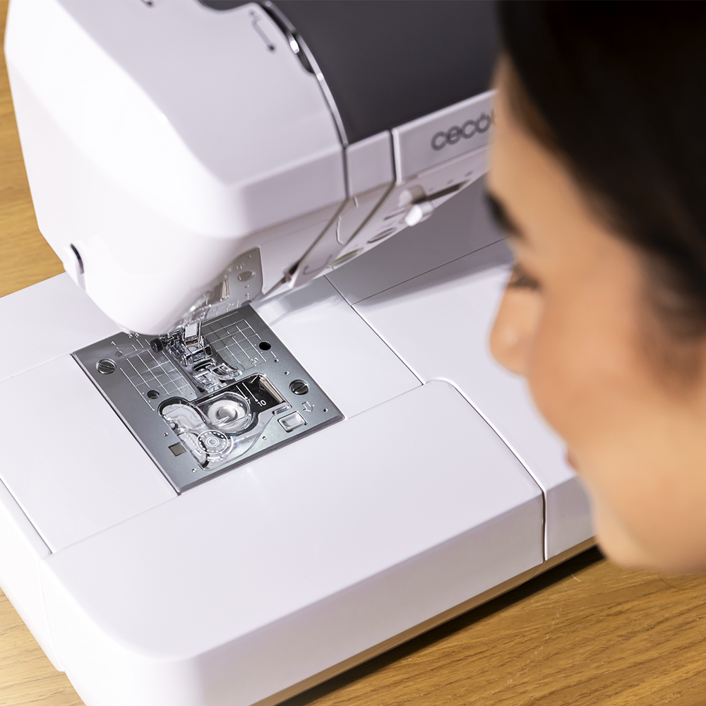 Una mujer mira una máquina de coser blanca con aguja y placa de metal.