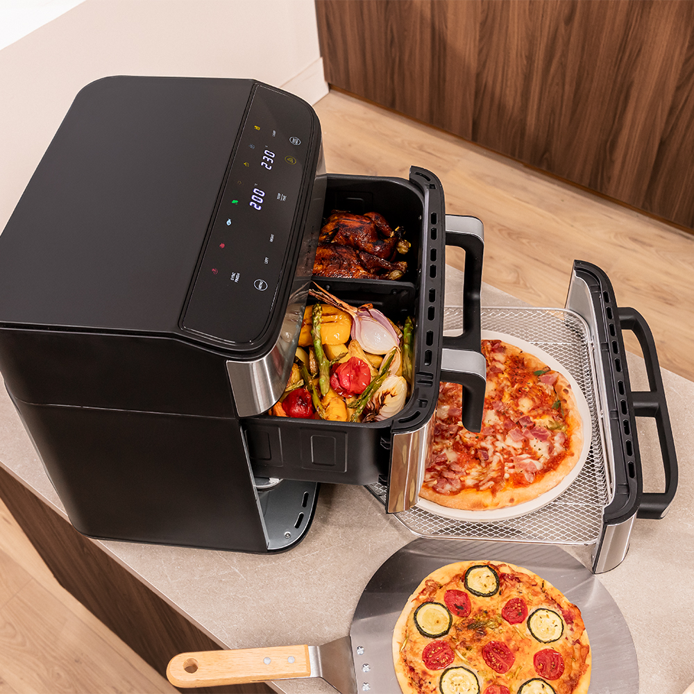 Una freidora de aire negra con pollo, verduras y dos pizzas.