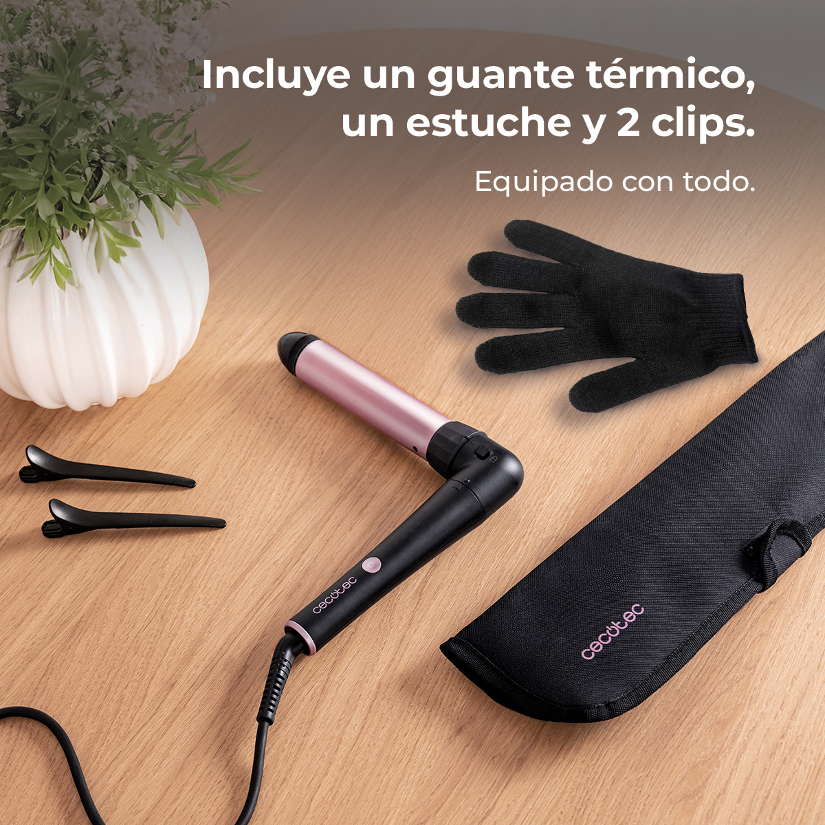 Un rizador rosa con mango negro, guante, estuche y pinzas en mesa madera.