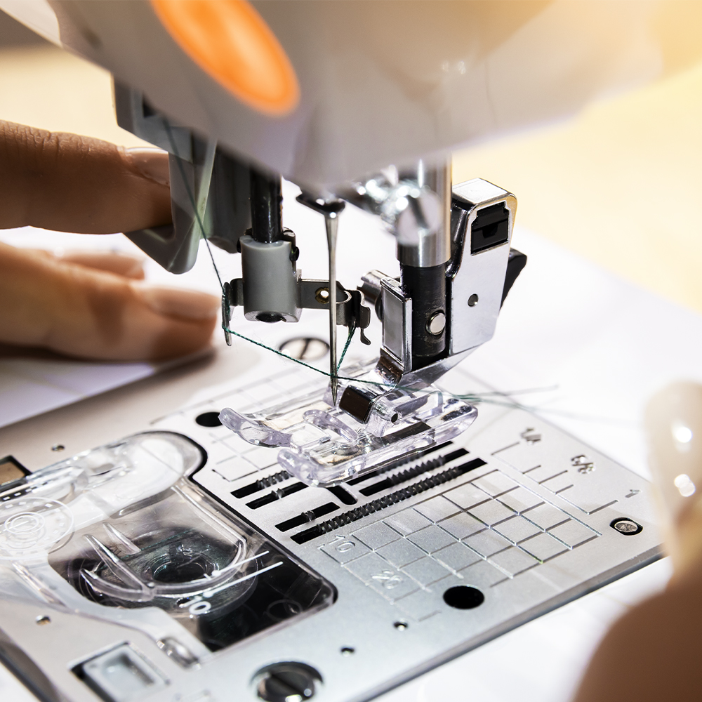 Primer plano del prensatelas de máquina de coser con aguja e hilo verde.
