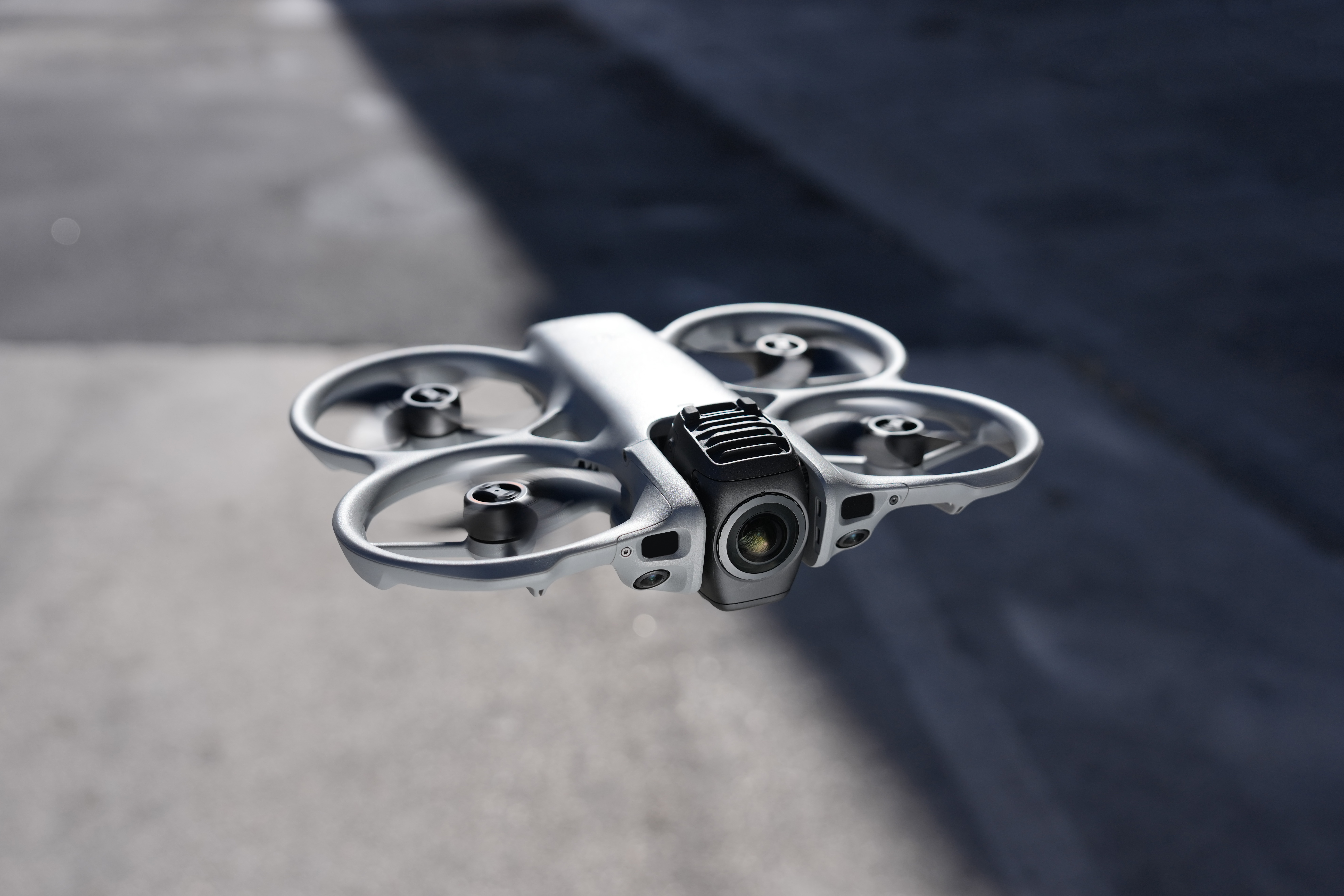 Ein silberner Quadrocopter schwebt vor einem unscharfen, grauen Hintergrund mit Schatten.
