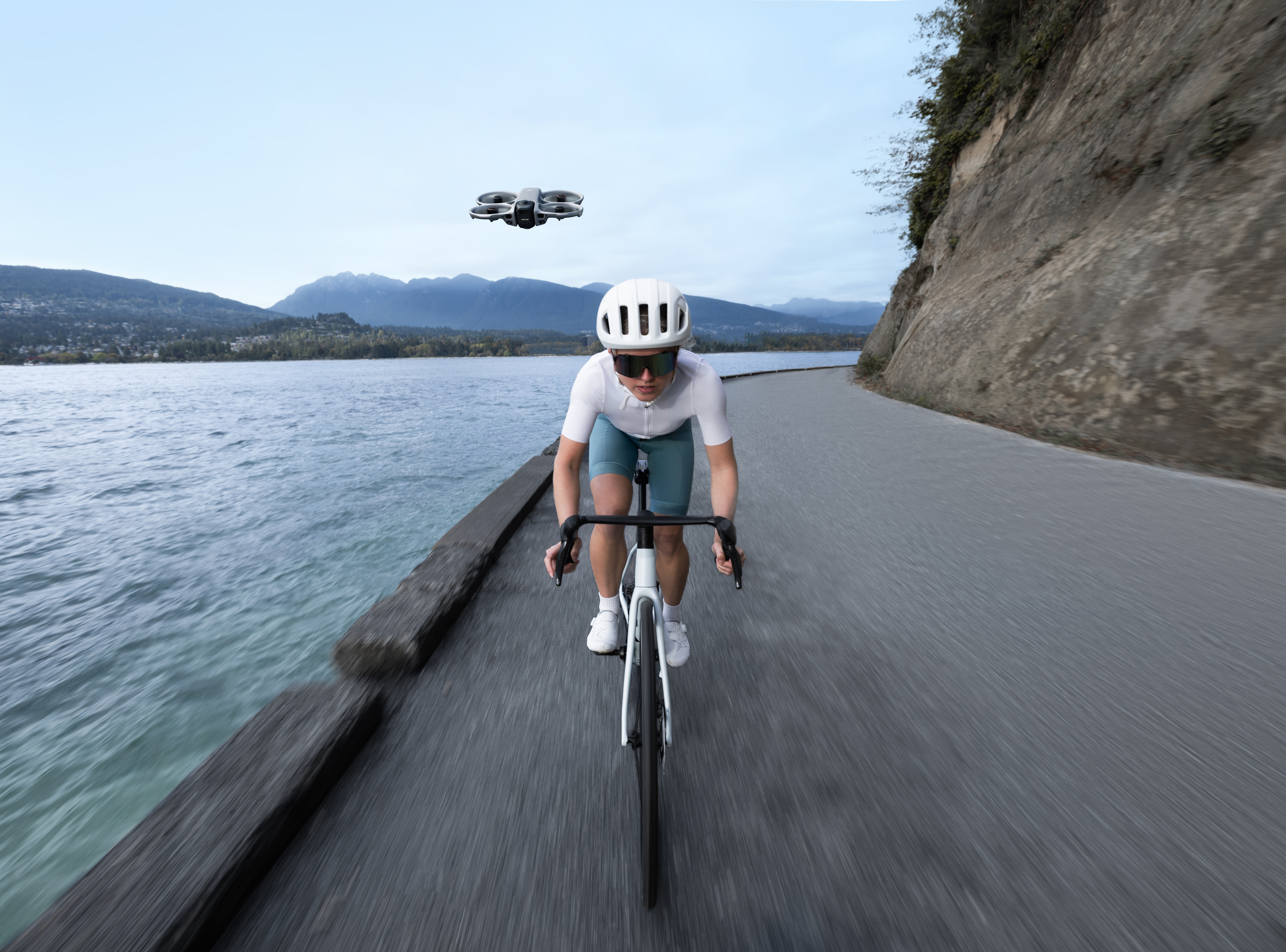 Ein Radfahrer fährt auf einer Straße neben einem See, eine Drohne fliegt über ihnen.
