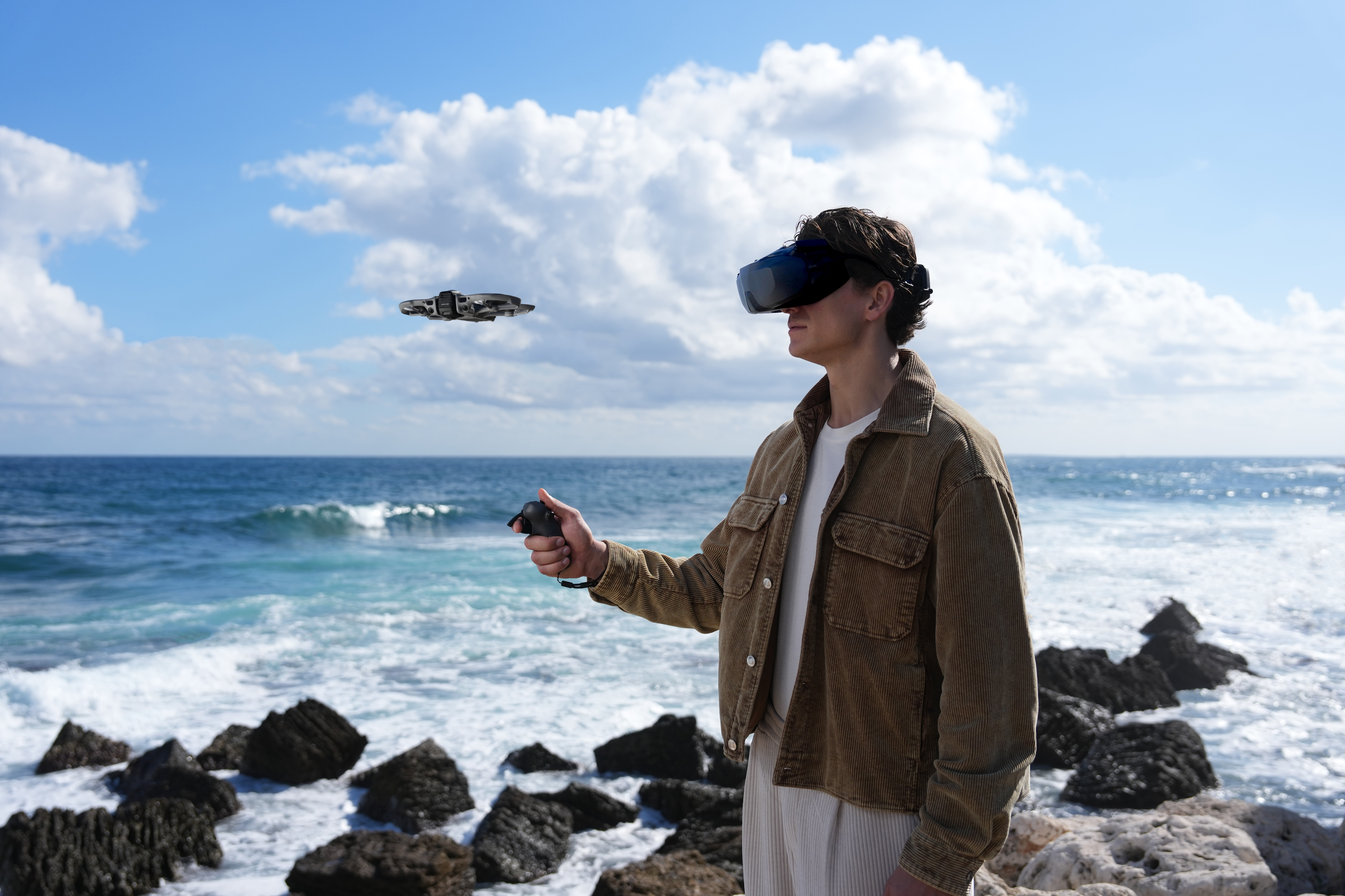 Mann mit VR-Brille steuert Drohne am Meer mit Felsen.