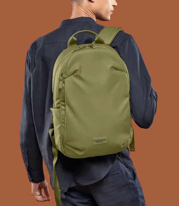 Un hombre lleva una mochila verde oliva sobre fondo naranja.