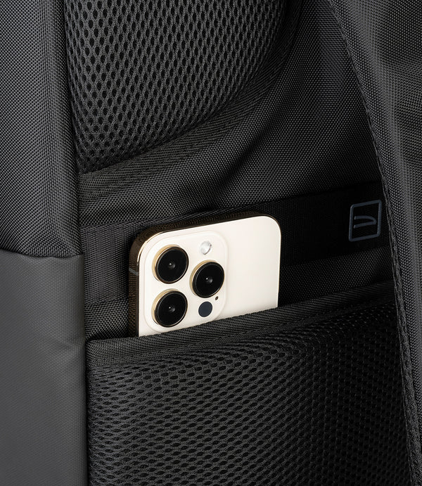 Un smartphone claro está guardado en un bolsillo de mochila negro con malla.