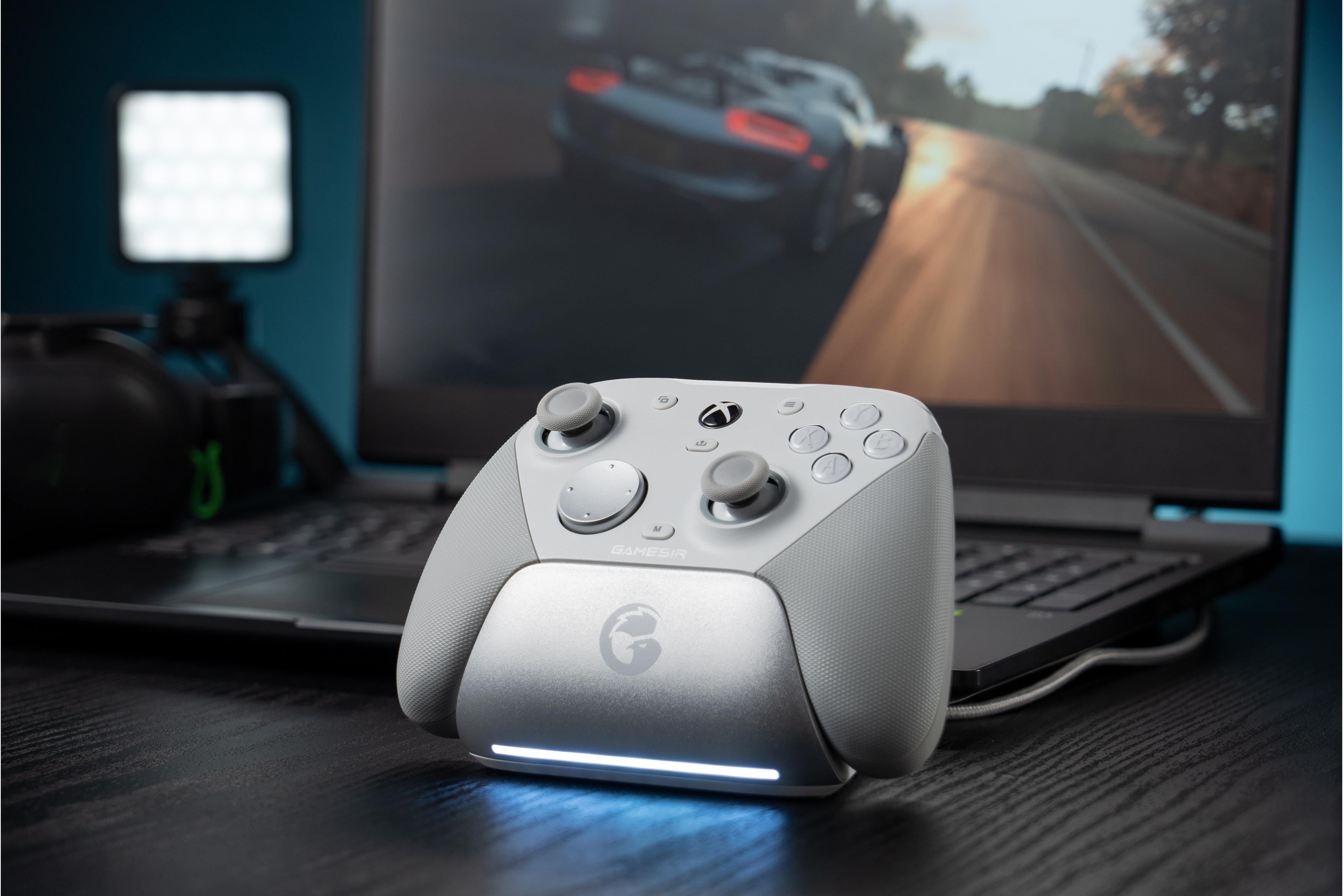 Un controller bianco poggia su una scrivania davanti a un laptop che mostra un gioco di corse.