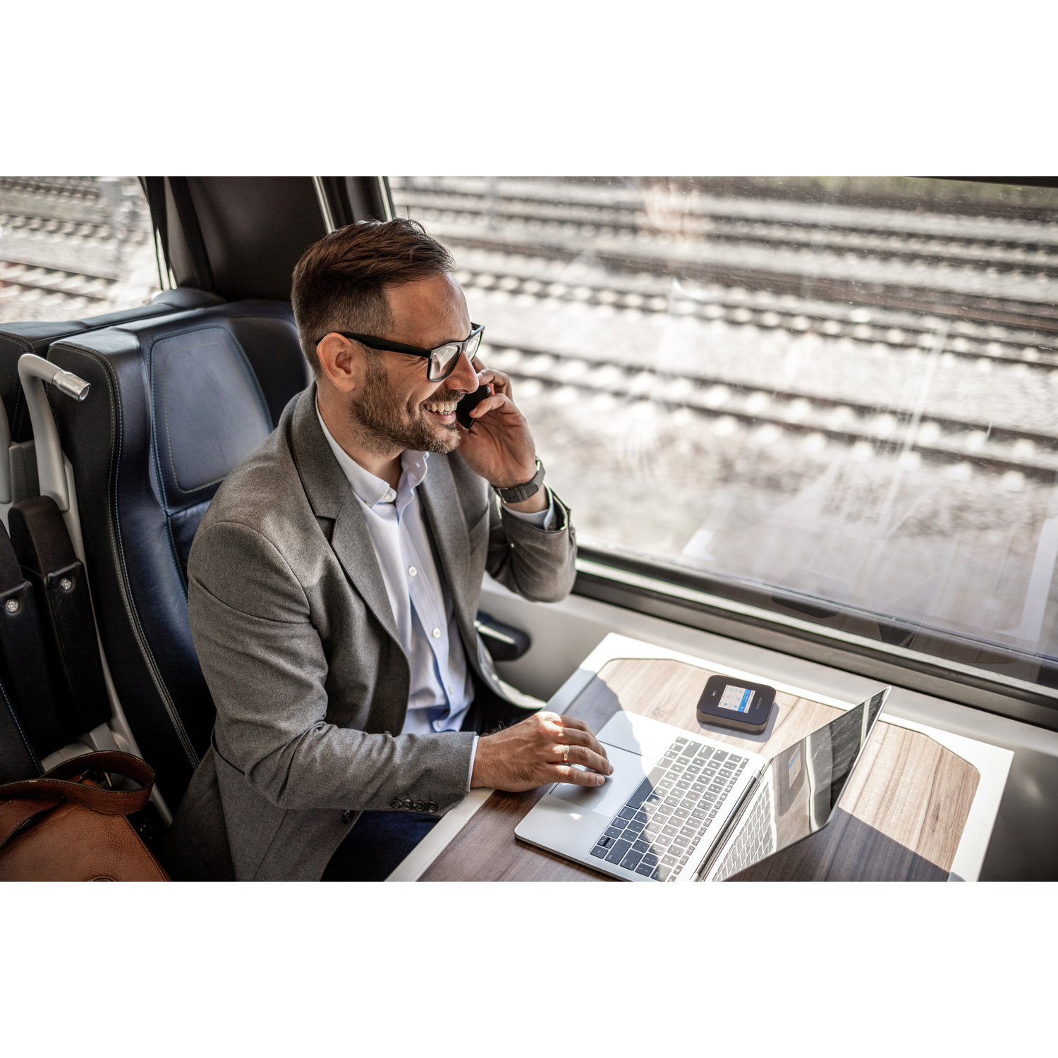 Man in pak belt in de trein, laptop en hotspot op tafel.