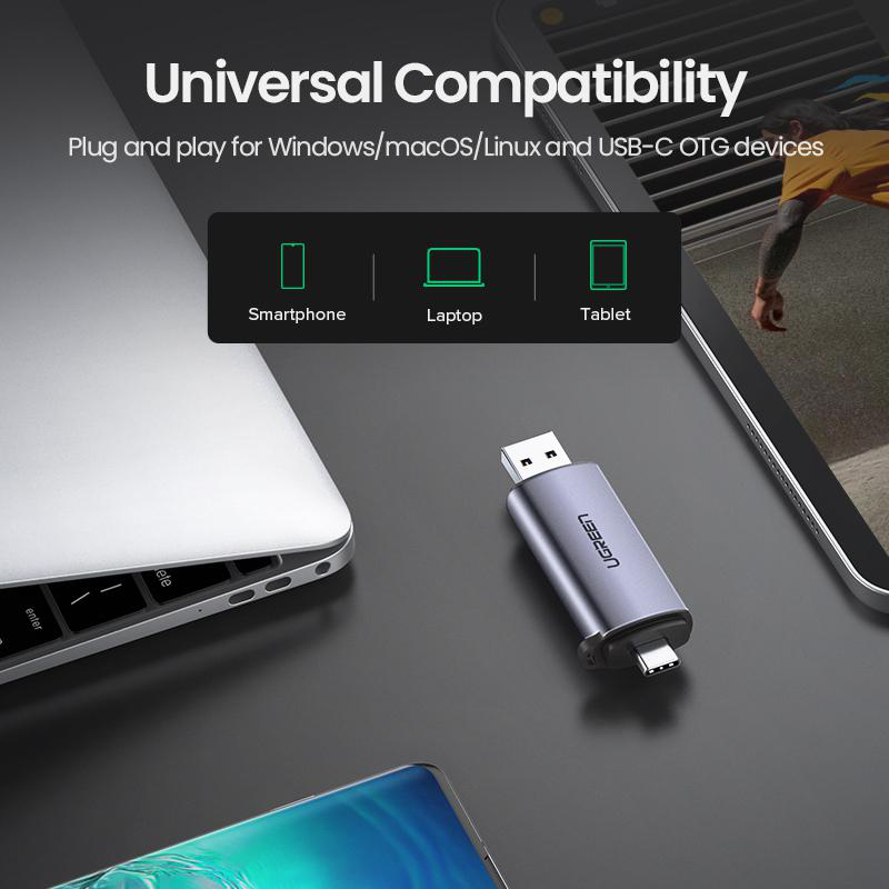 Ein grauer USB-C-Adapter liegt neben einem Laptop und einem Smartphone. Kompatibel mit vielen Geräten.