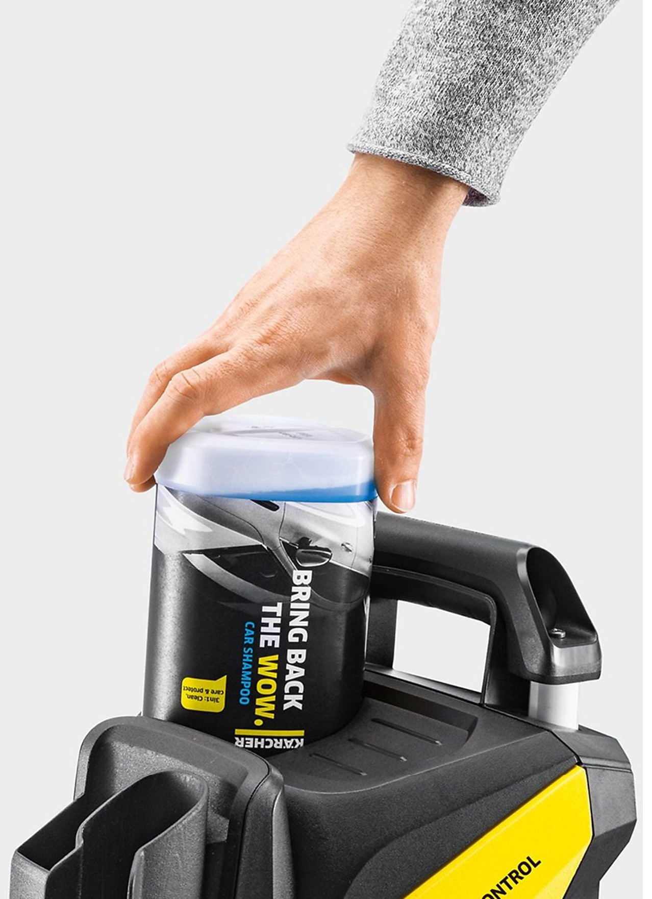 Ręka trzyma butelkę szamponu samochodowego na myjce ciśnieniowej.