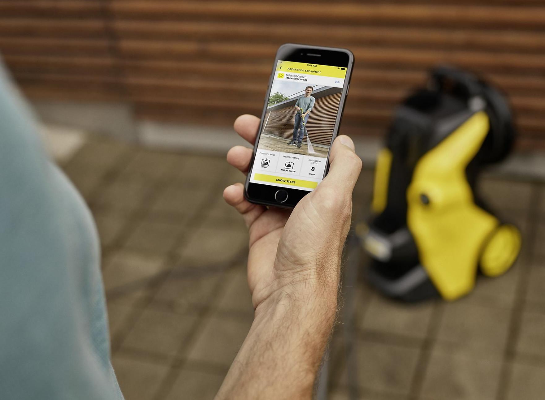 Mężczyzna trzyma smartfon z aplikacją do czyszczenia kamiennych podłóg. Urządzenie Kärcher.
