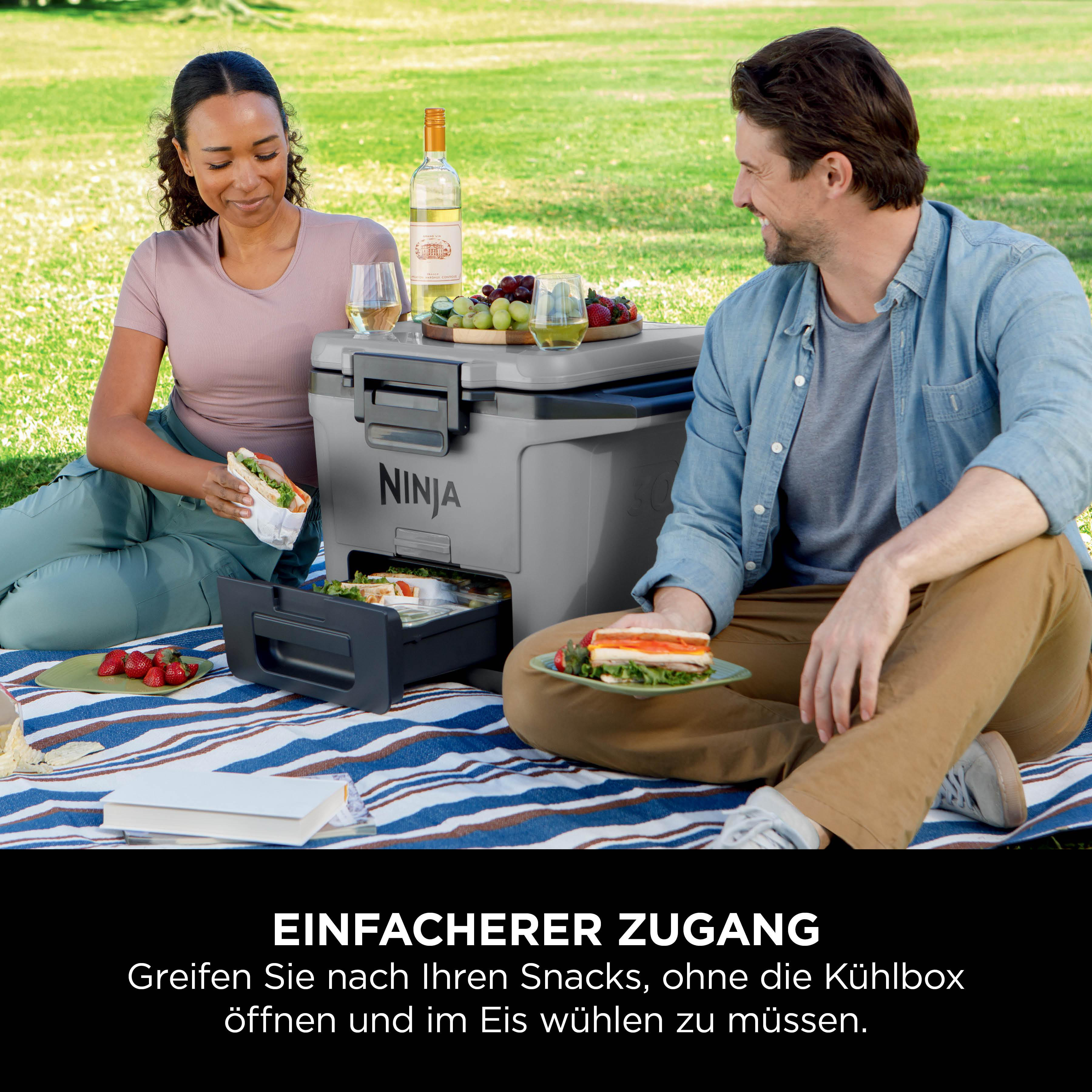 Paar beim Picknick mit Kühlbox und Snacks im Gras.