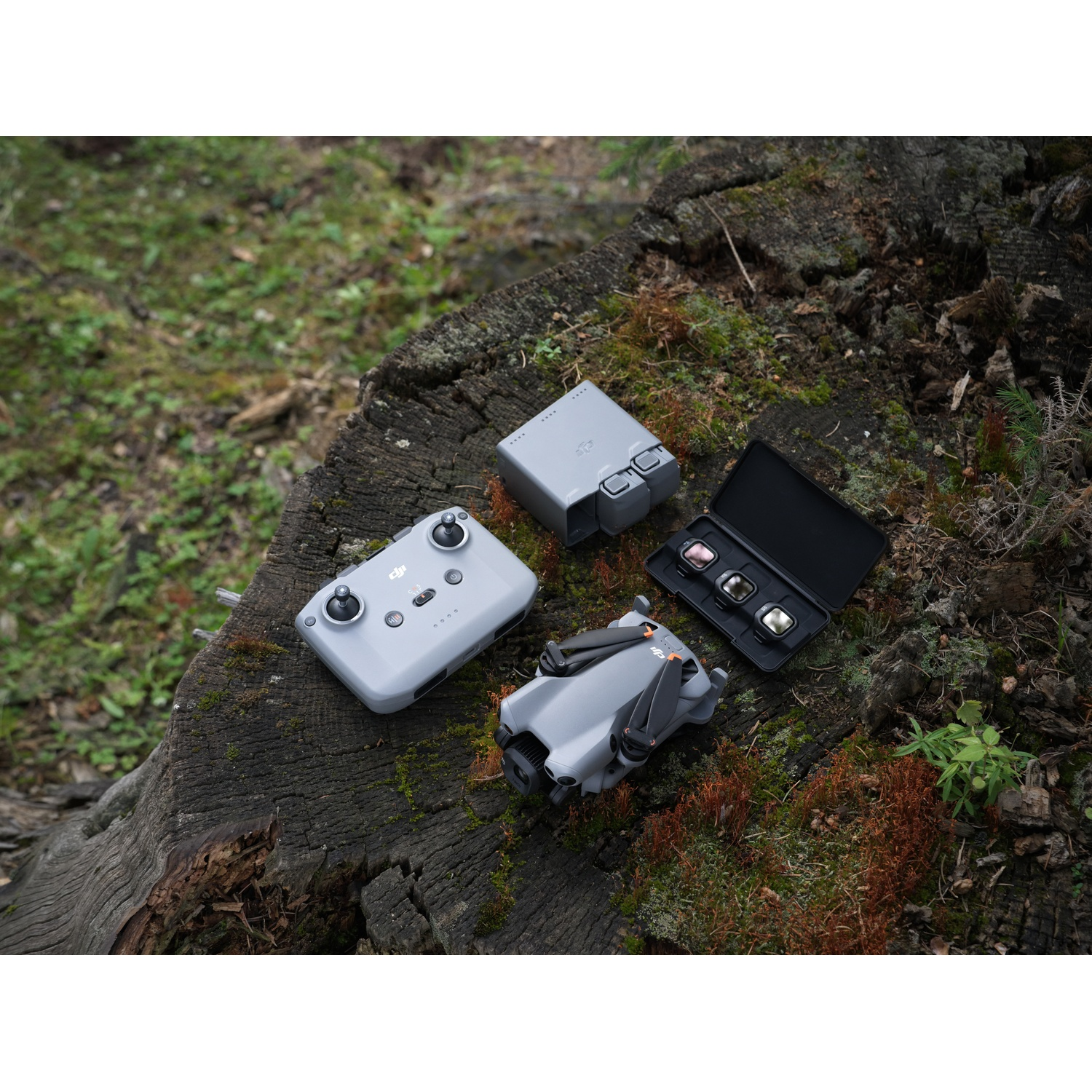 Gray drone, remote, and filters on a tree stump outdoors.