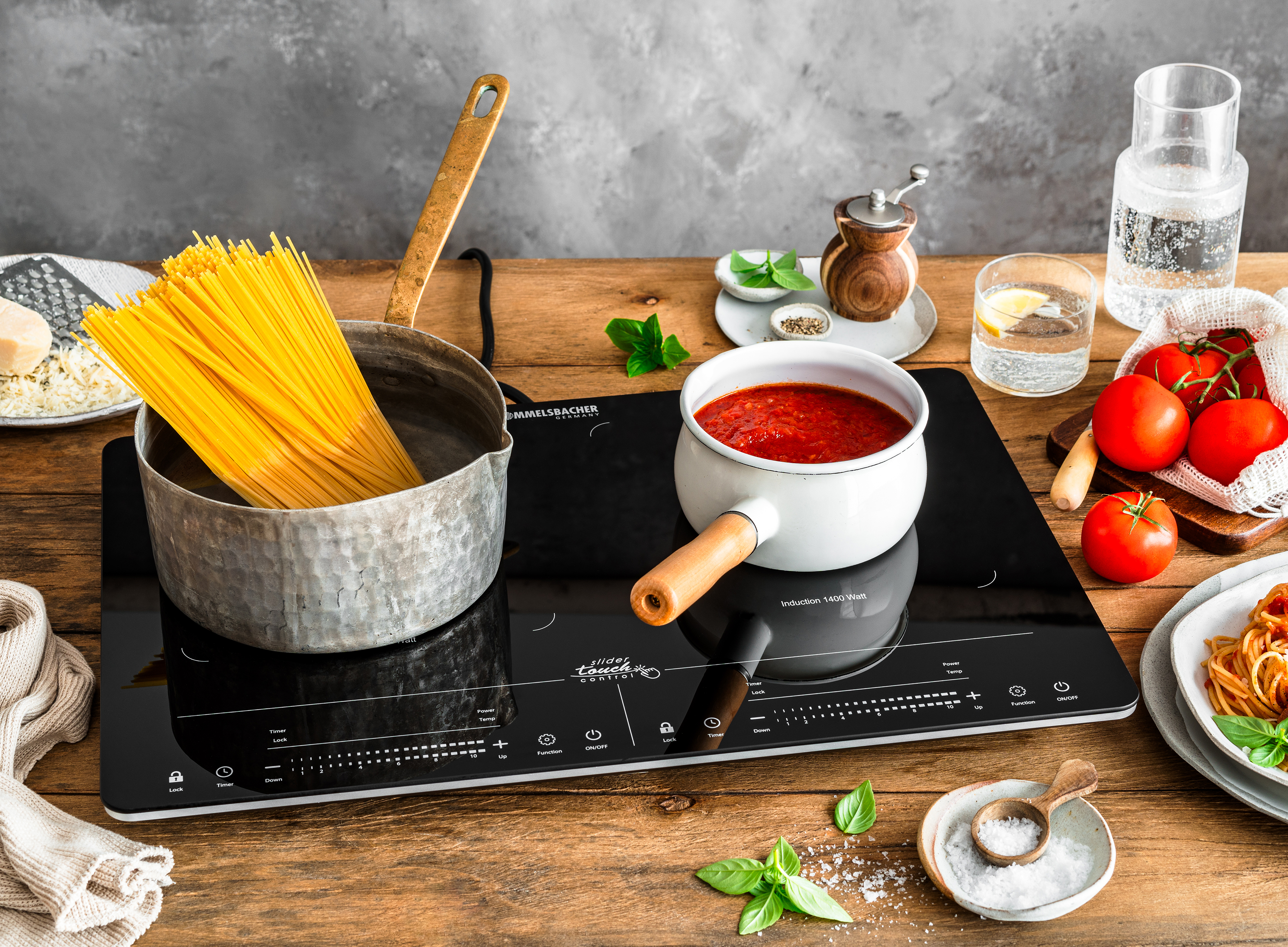Spaghetti kochen mit Tomatensoße auf einem Induktionskochfeld mit Kochutensilien.