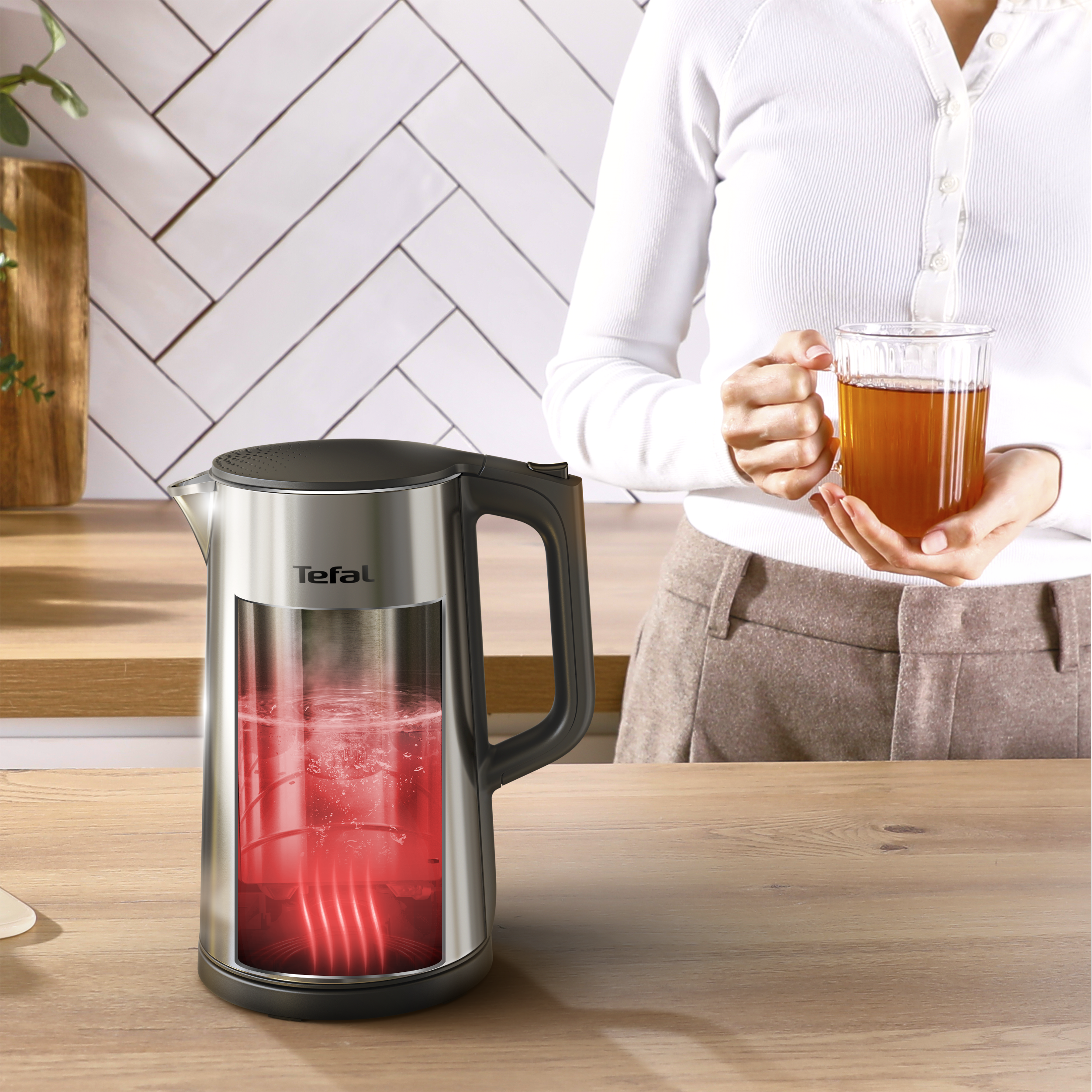 Egy Tefal vízforraló világító vízzel egy teát tartó személy mellett.