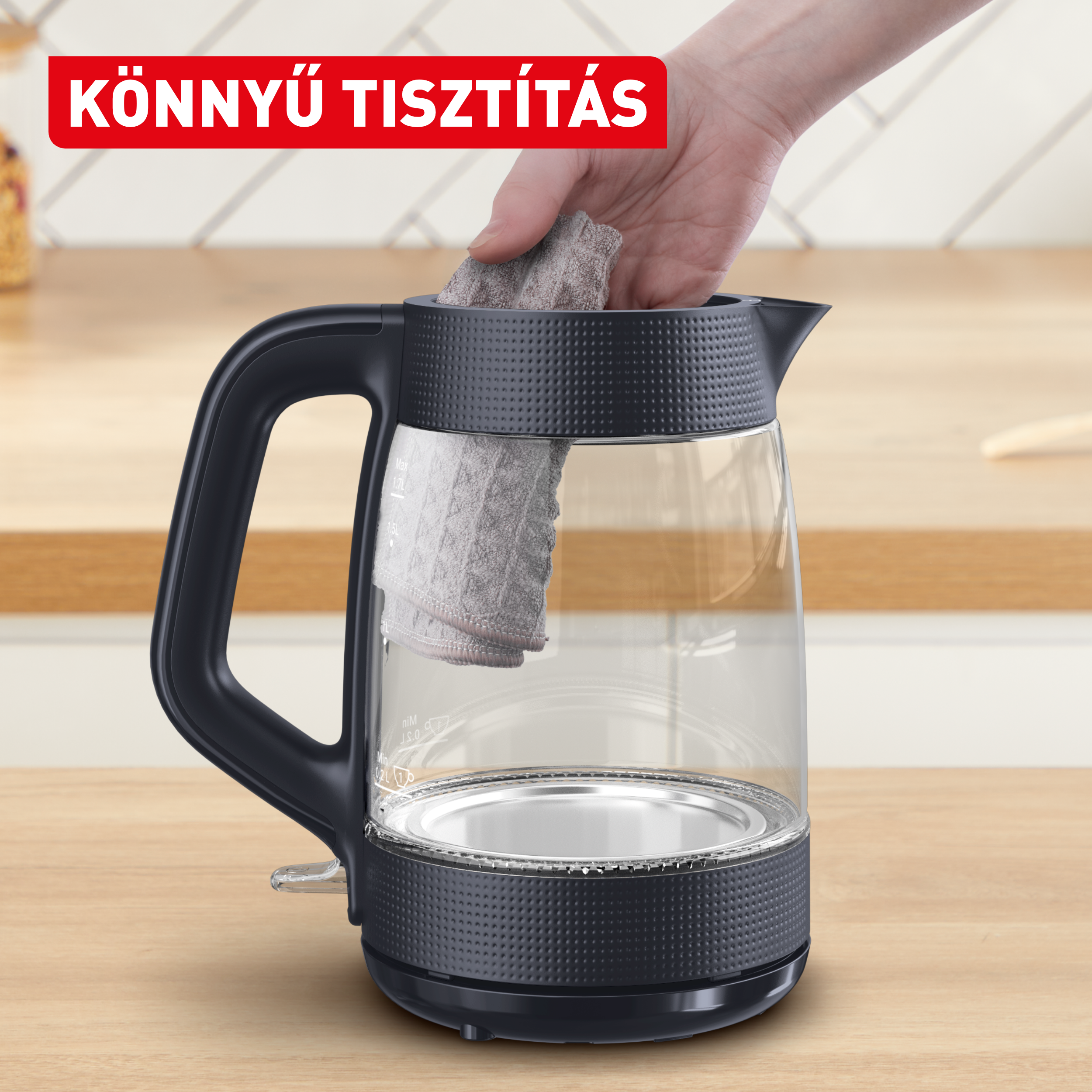 Egy kéz tisztít egy üveg vízforralót szürke ruhával. Piros felirat felül.