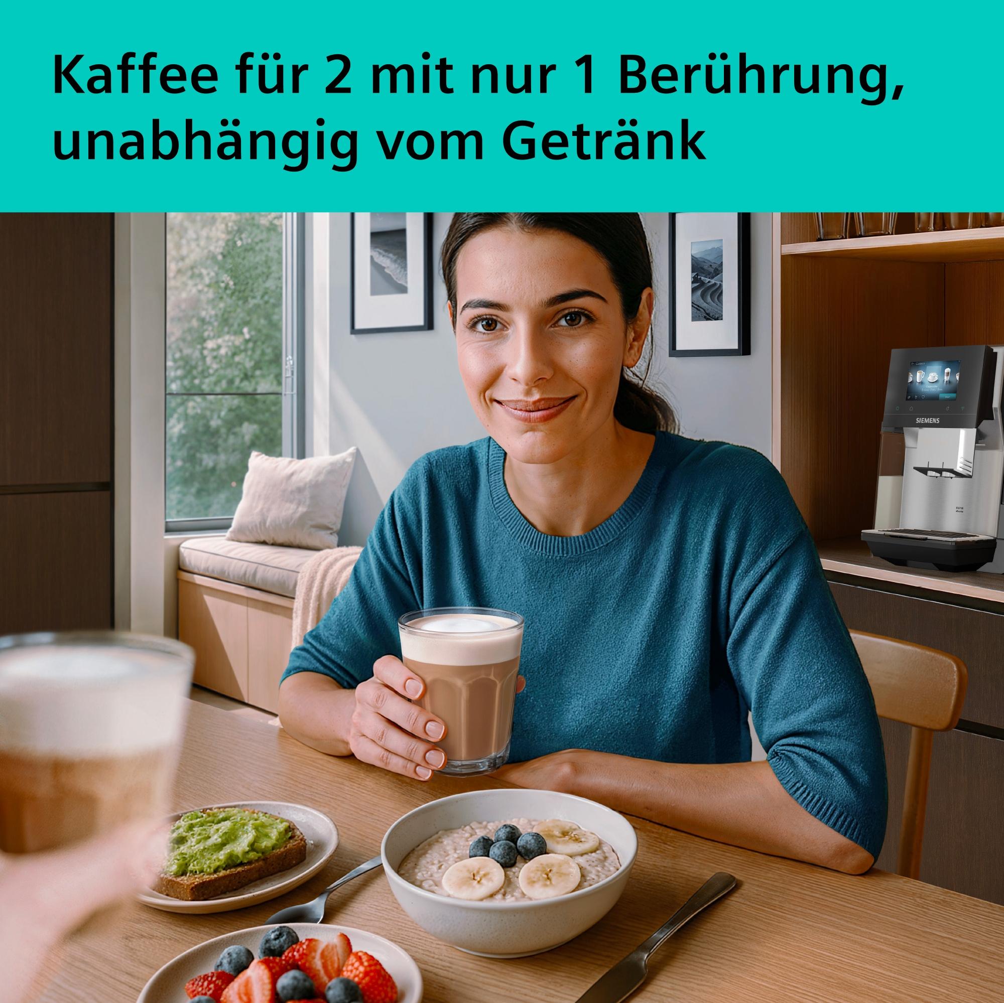 Frau hält Kaffee, Frühstück mit Obst und Haferflocken. Kaffeemaschine im Hintergrund.