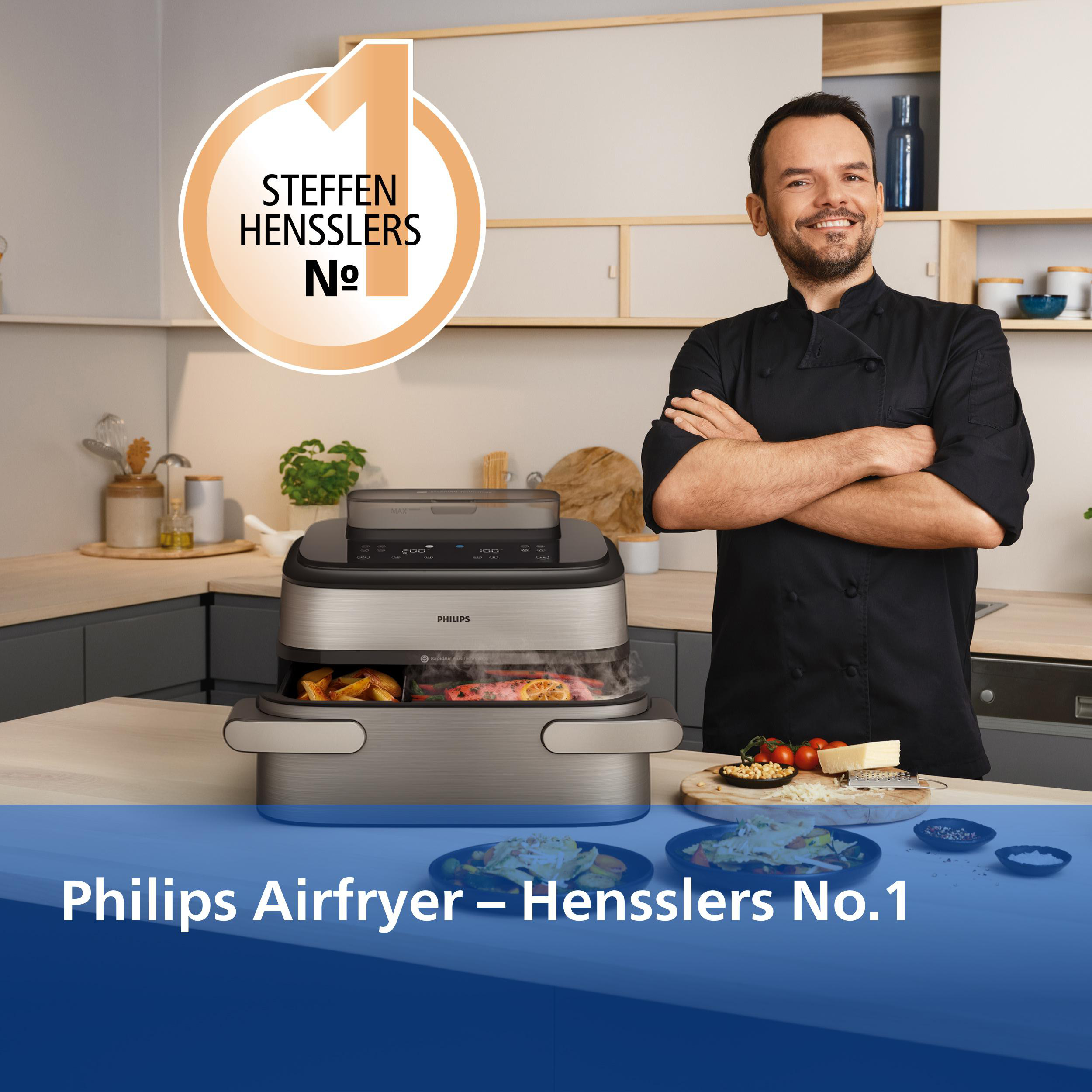 Ein Koch in schwarzer Kleidung steht neben einem Philips Airfryer mit Essen darin.