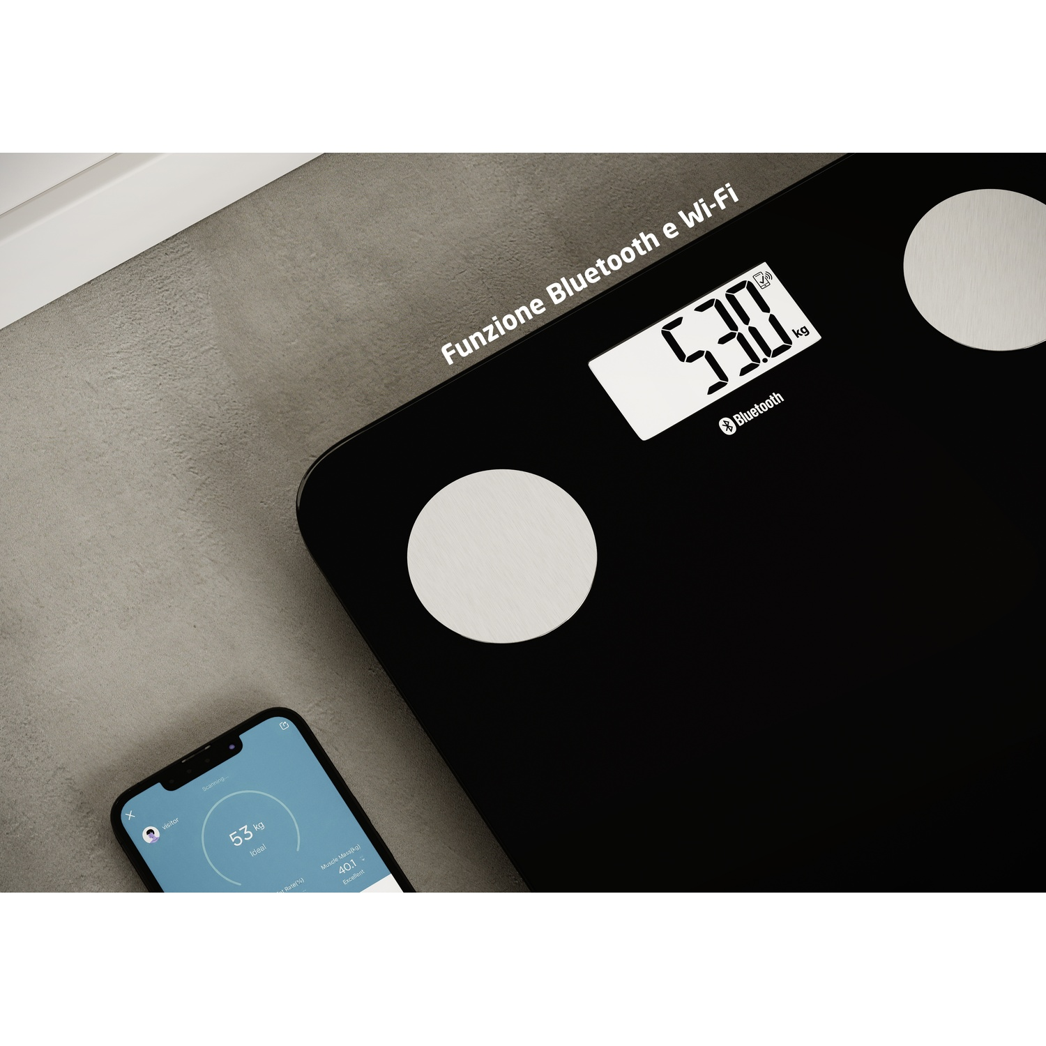 Bilancia nera con display mostra 53,0 kg. Smartphone accanto mostra 53 kg.