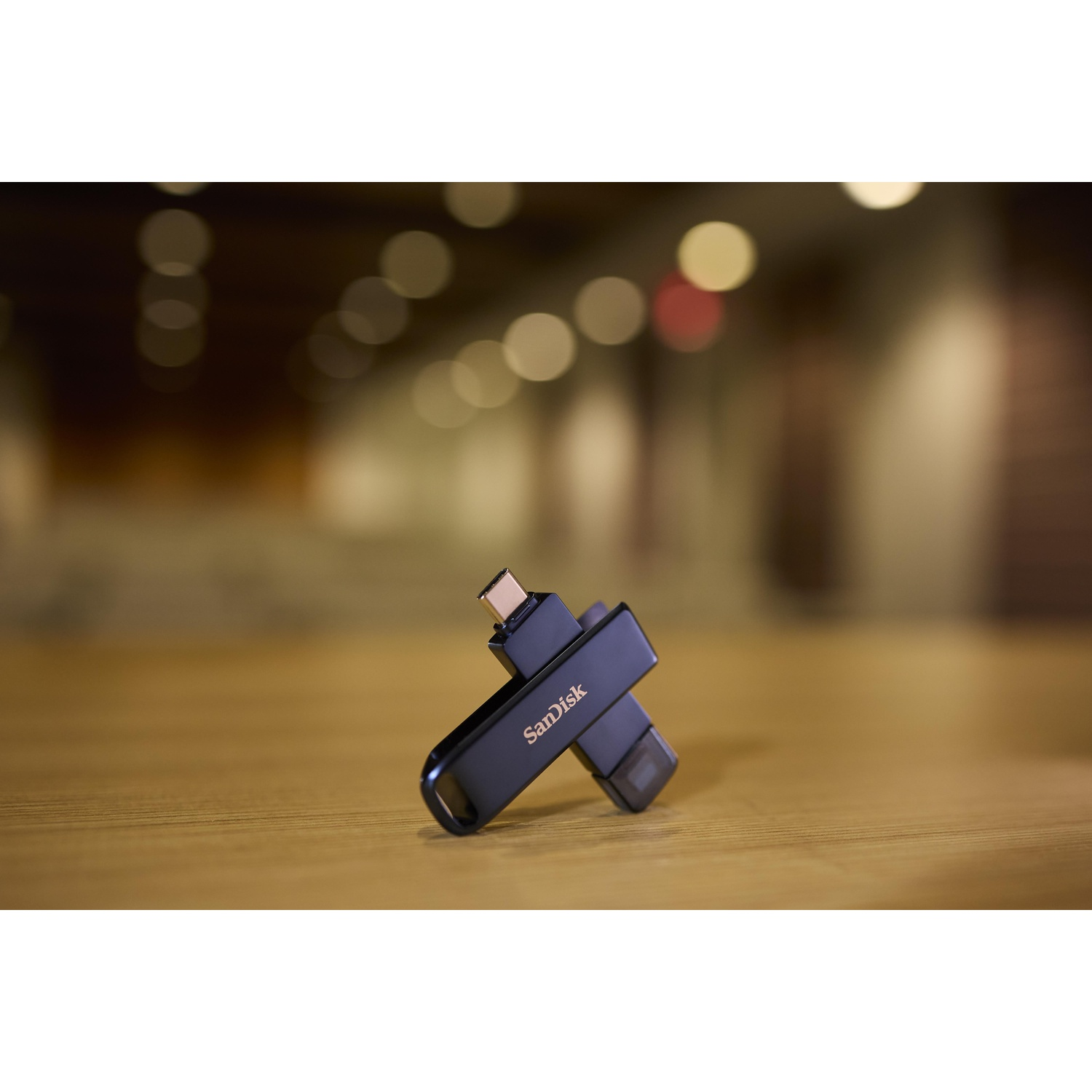 Un'unità USB SanDisk nera a doppio connettore poggia su un tavolo di legno.