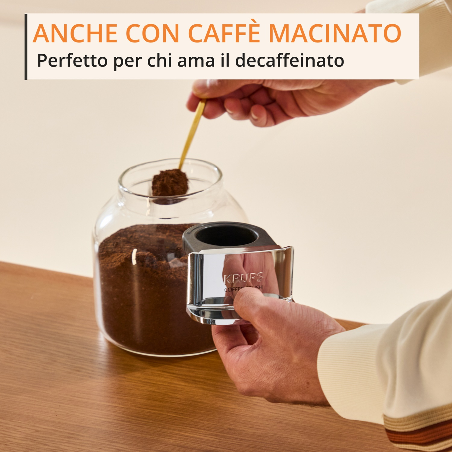 Una mano solleva un cucchiaio di caffè macinato da un barattolo.