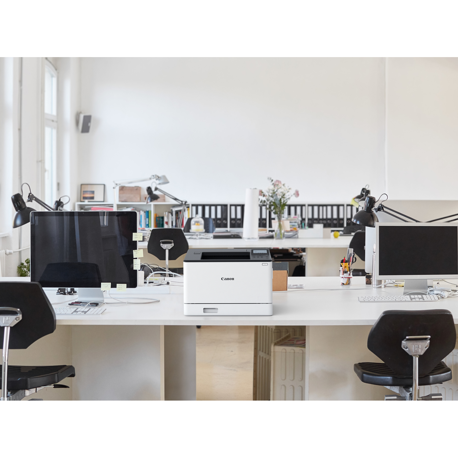 A Canon printer sits on a white desk in a modern office.