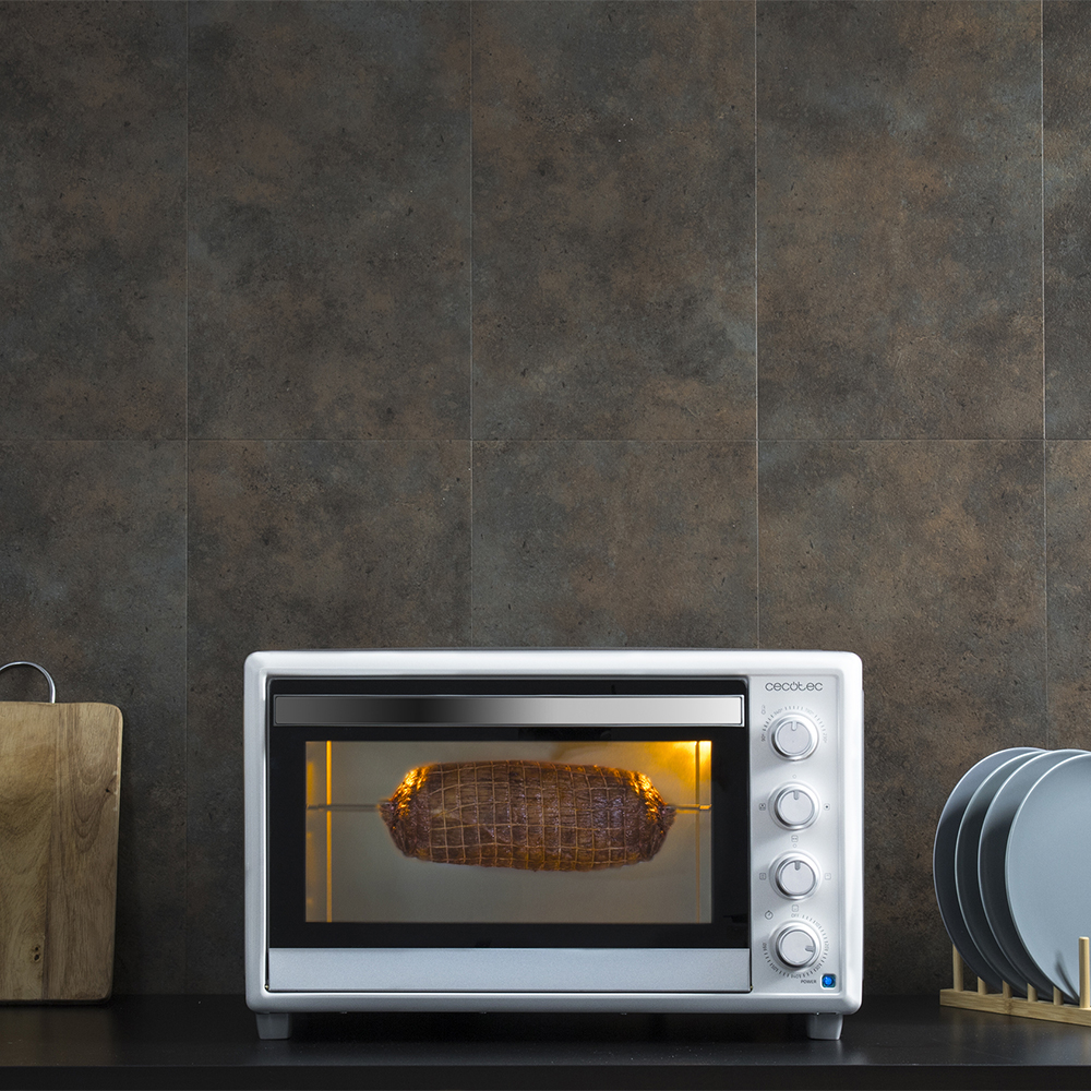 Un asado en red gira en un horno blanco contra azulejos oscuros.
