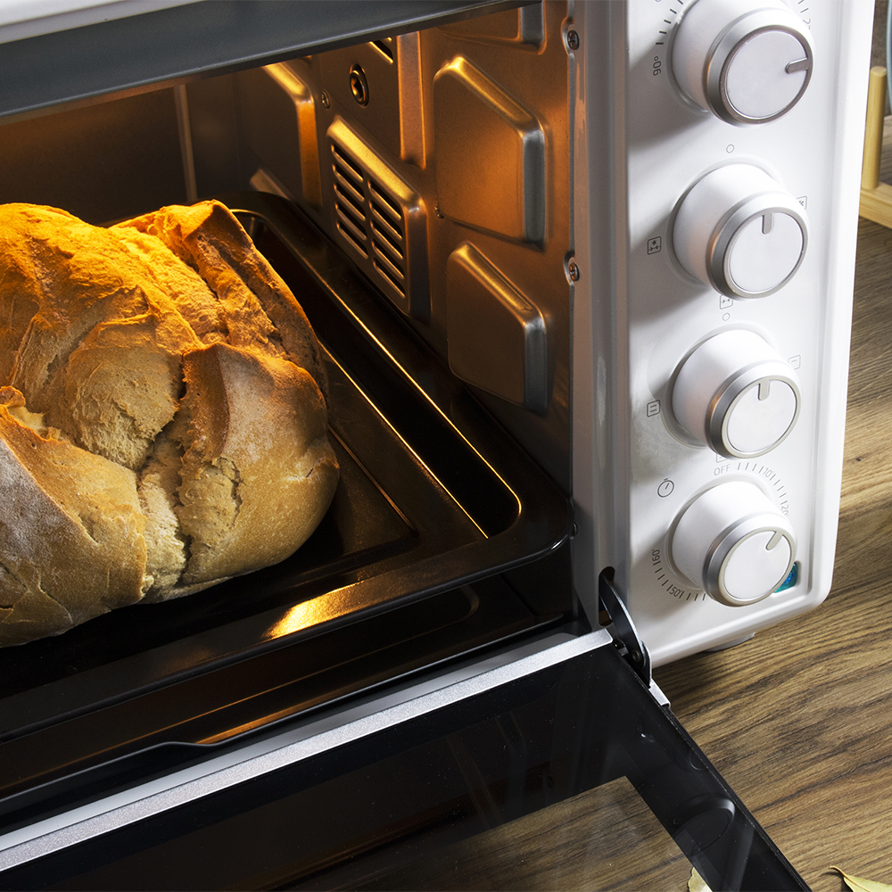 Una hogaza de pan dorada se hornea en un horno blanco abierto en una bandeja.