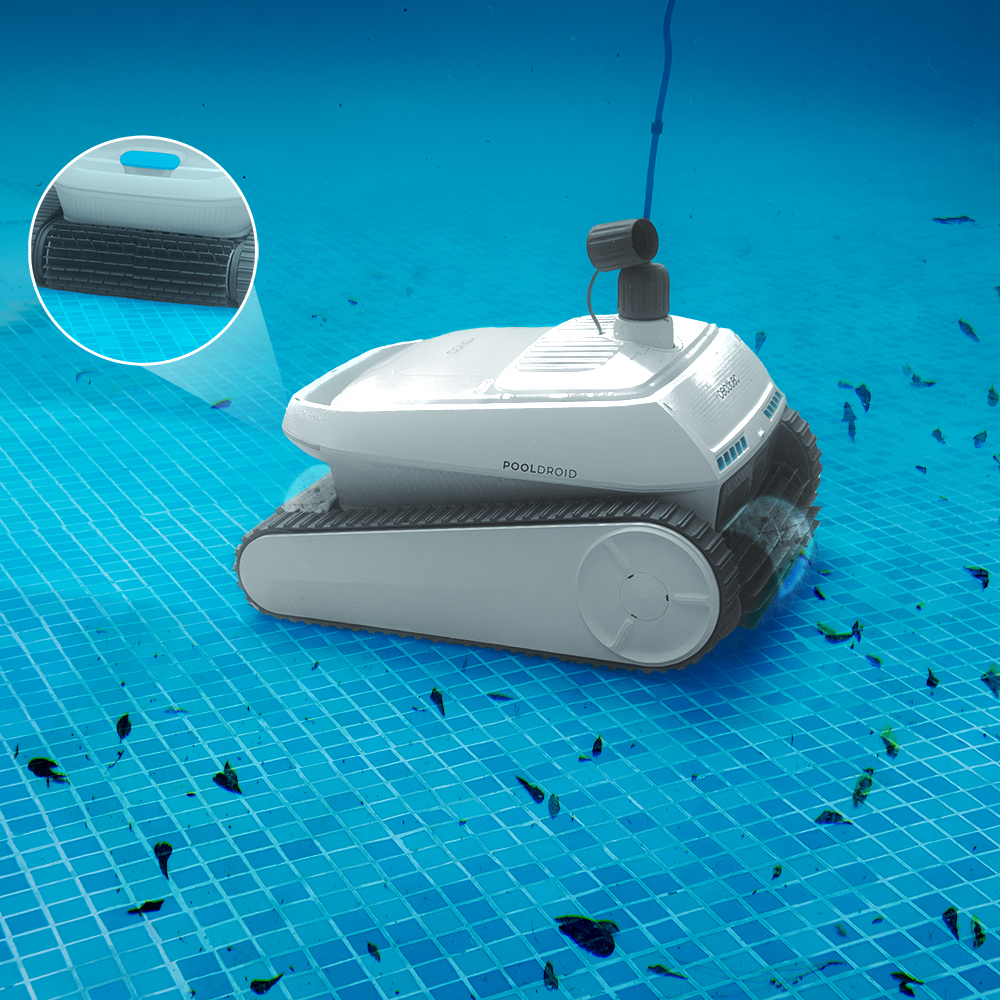 Un robot blanco para piscina con orugas limpia una piscina azul, recogiendo escombros.