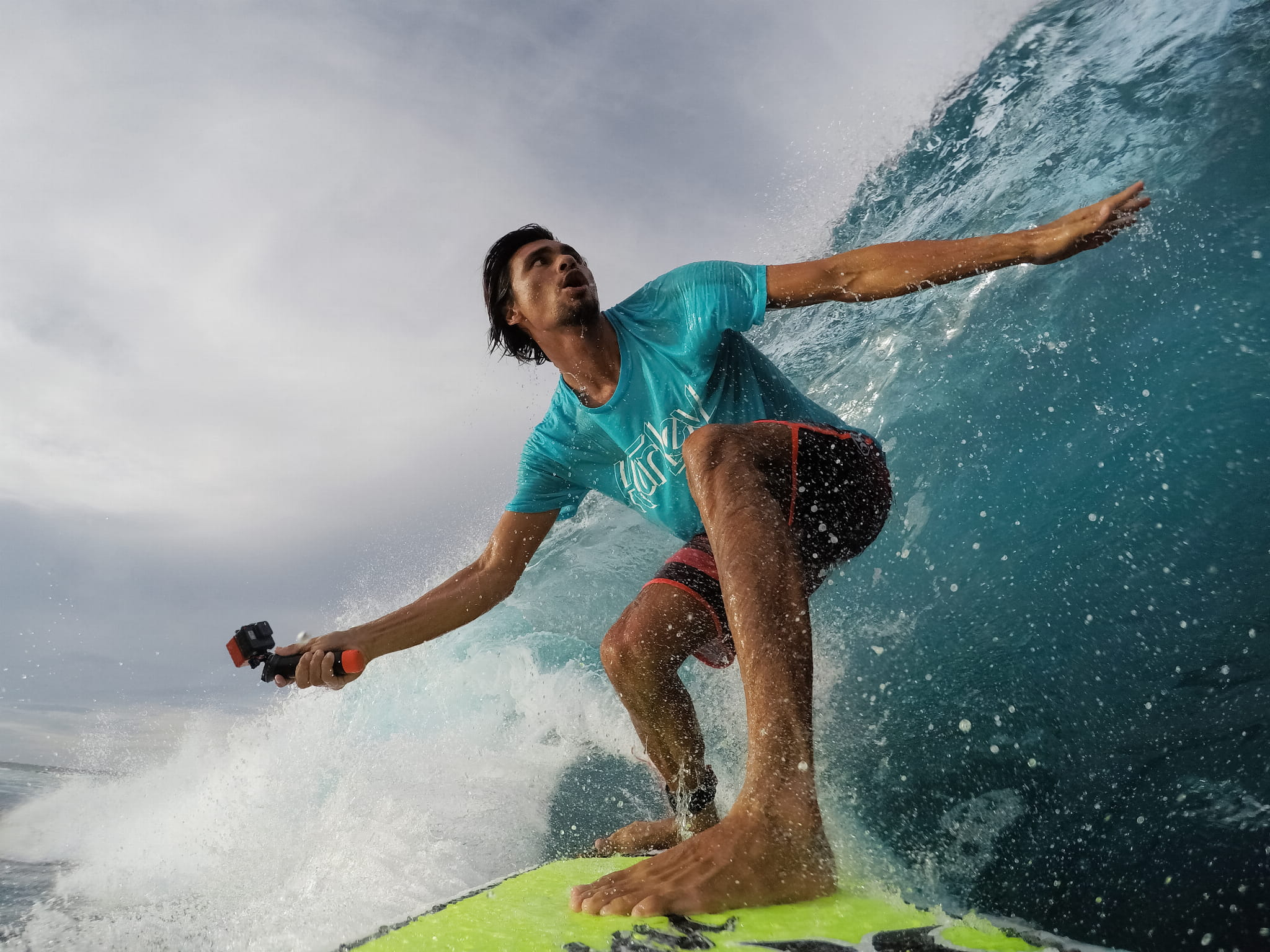 Surfer jedzie na fali z kamerą. Niebieska woda i niebo.