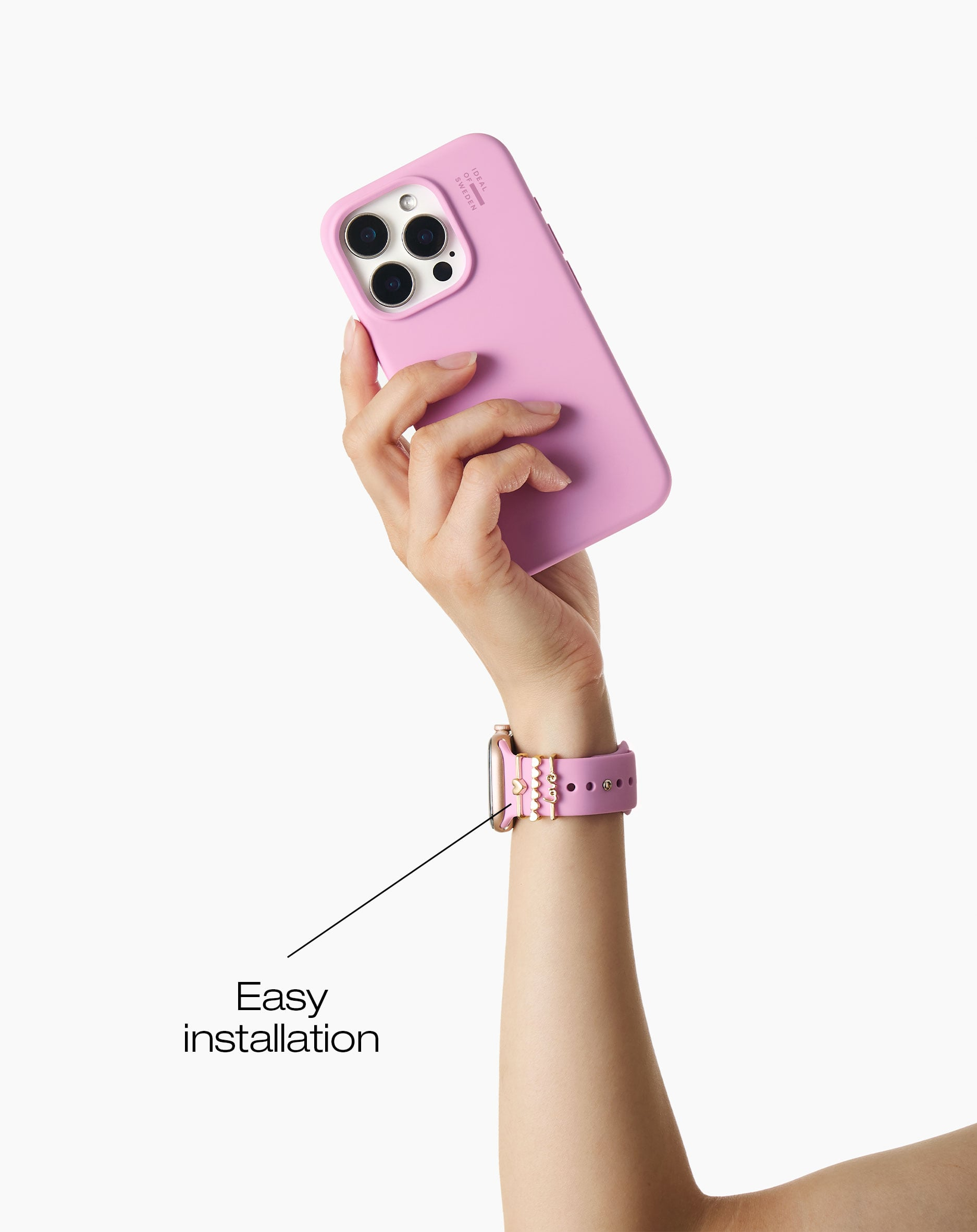 Eine Hand hält ein rosafarbenes Handy, während eine rosafarbene Uhr mit Herzanhängern am Handgelenk getragen wird.