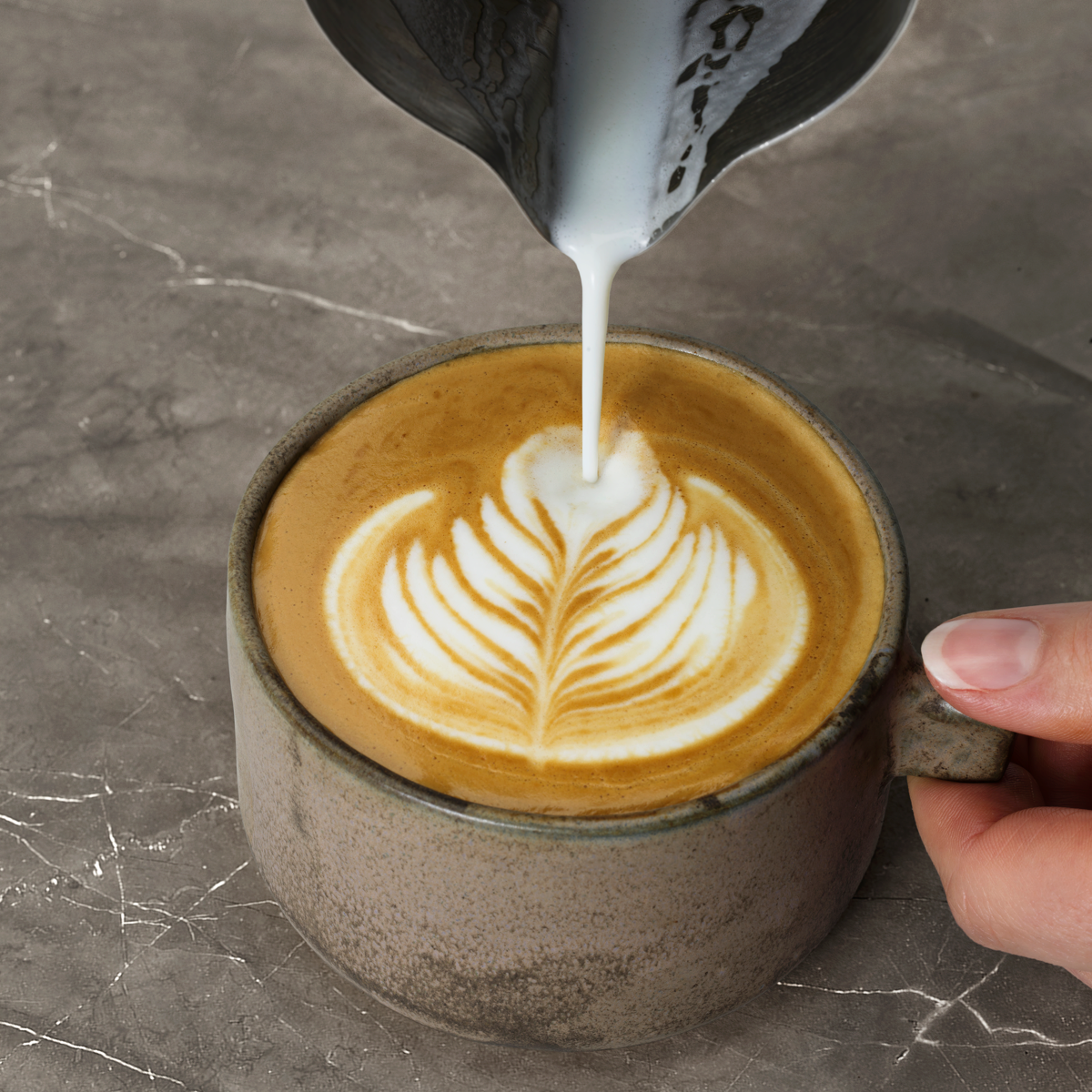 Bir masadaki latte art kahveye süt dökülüyor.