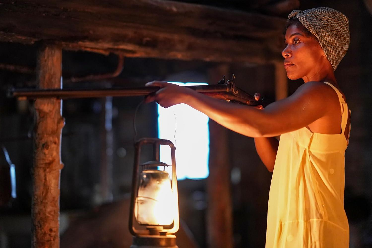 Frau mit Gewehr und Laterne in dunkler Hütte.