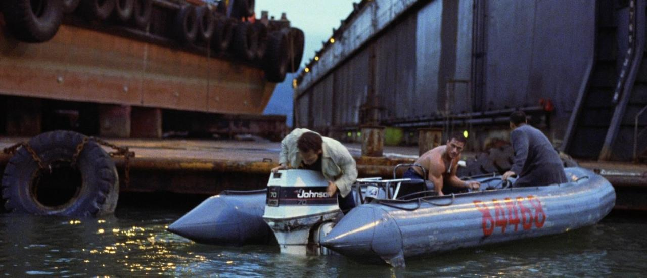 Männer in Schlauchboot mit Außenbordmotor vor einem Dock.